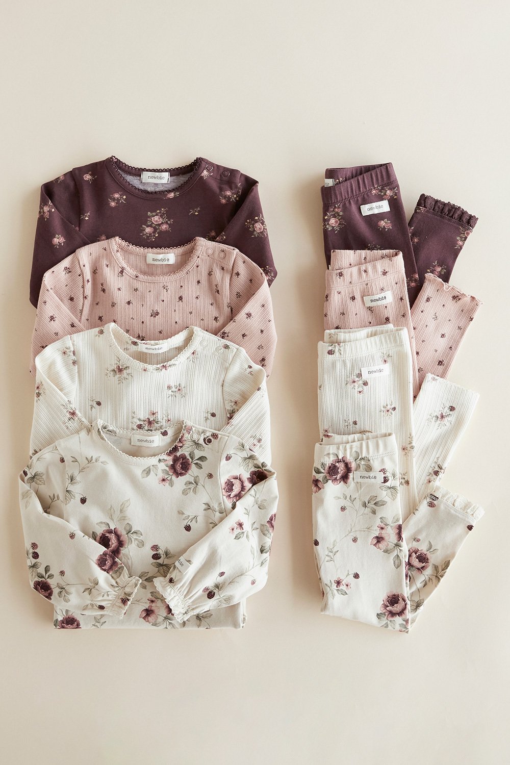 Gefaltete Babyoberteile und Leggings in Rosa, Creme und Pflaume mit Blumenmuster.
