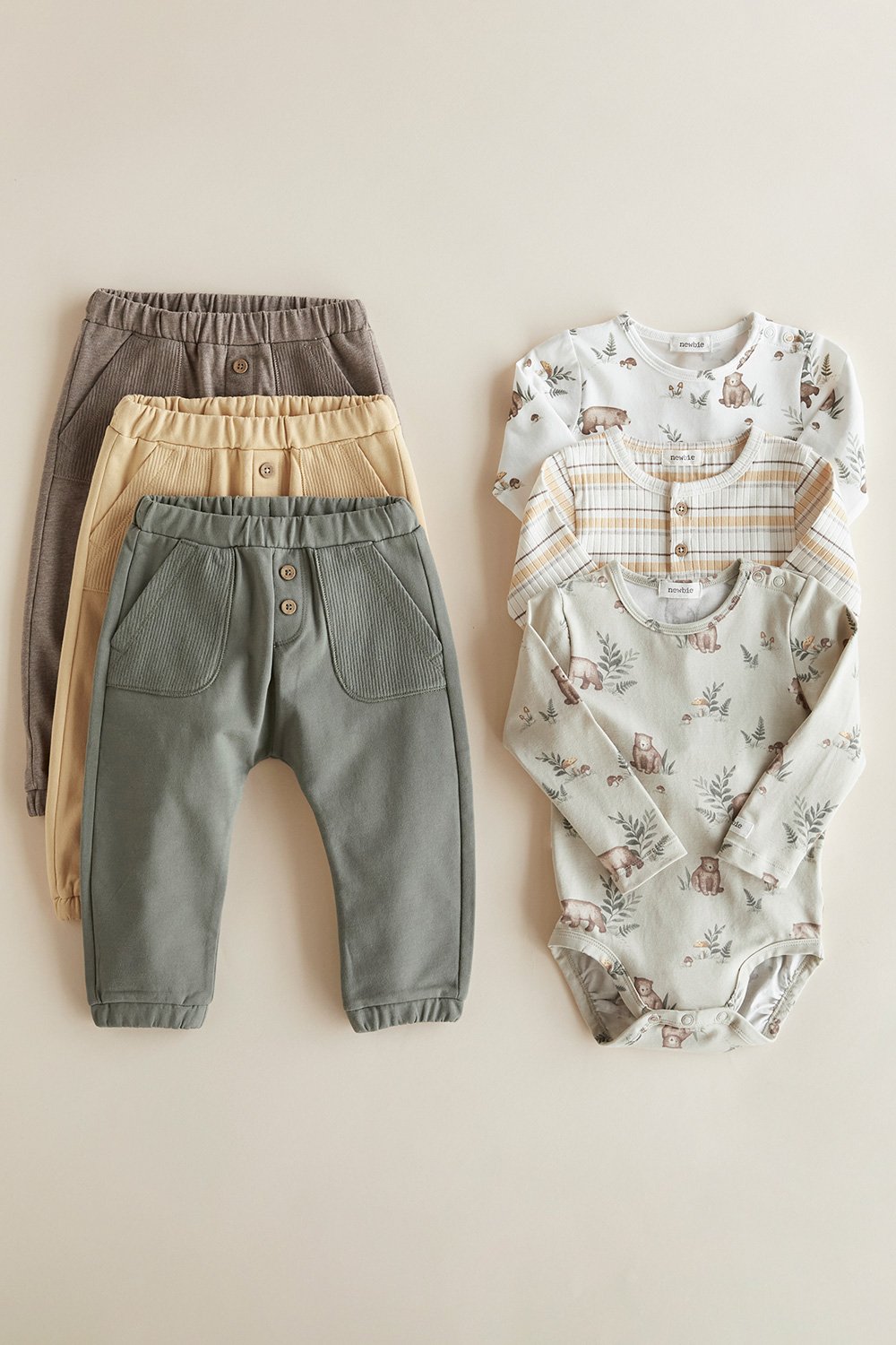 Kinderhosen in Grün, Gelb und Taupe neben Babybodys mit Bärenmotiven.