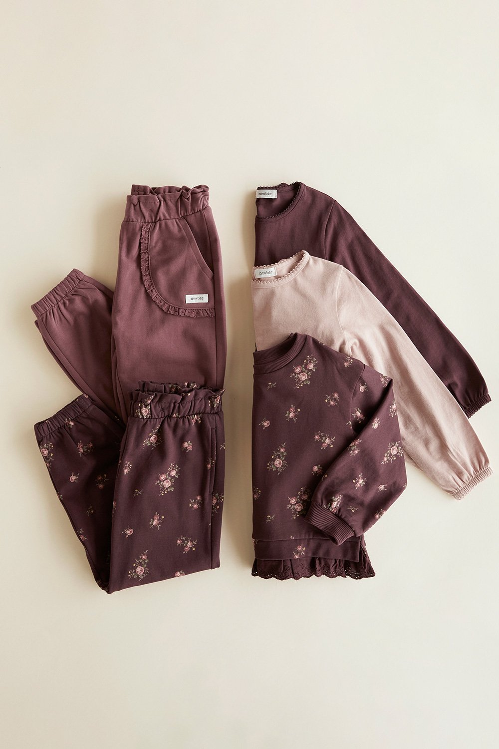 Gefaltete Kinderoberteile und Hosen in Pflaumen- und Rosatönen mit Blumenmuster.