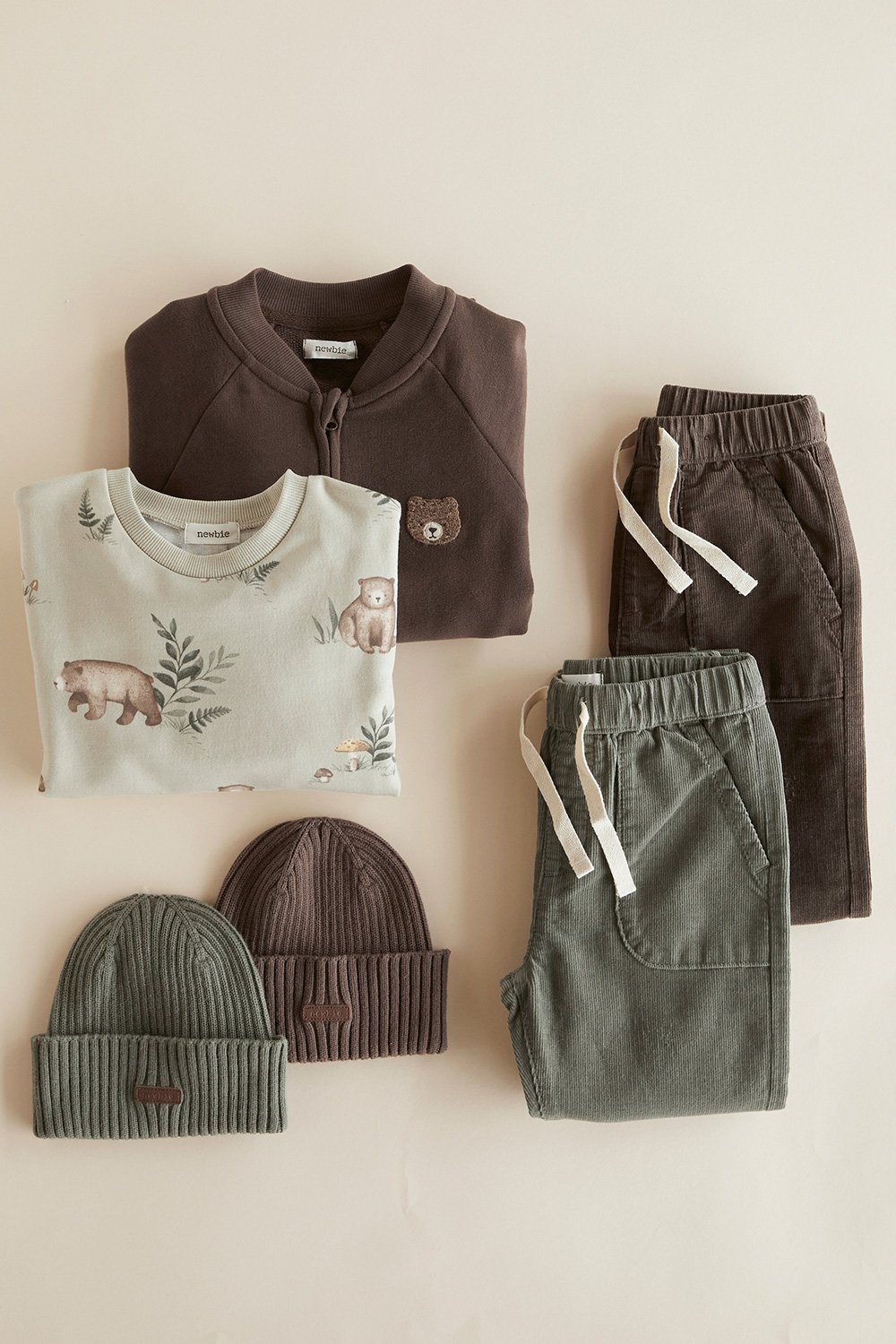 Gefaltetes Kinder-Sweatshirt mit Bärenmotiv, Cordhosen und Strickmützen in Naturtönen.