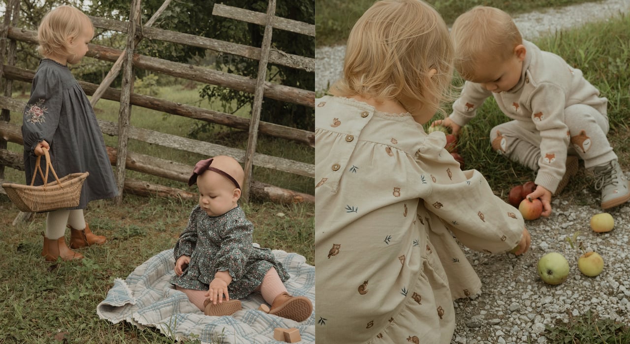 Zwei kleine Kinder in gemusterten Kleidern im Freien an einem rustikalen Holzzaun mit Körben und Decke.