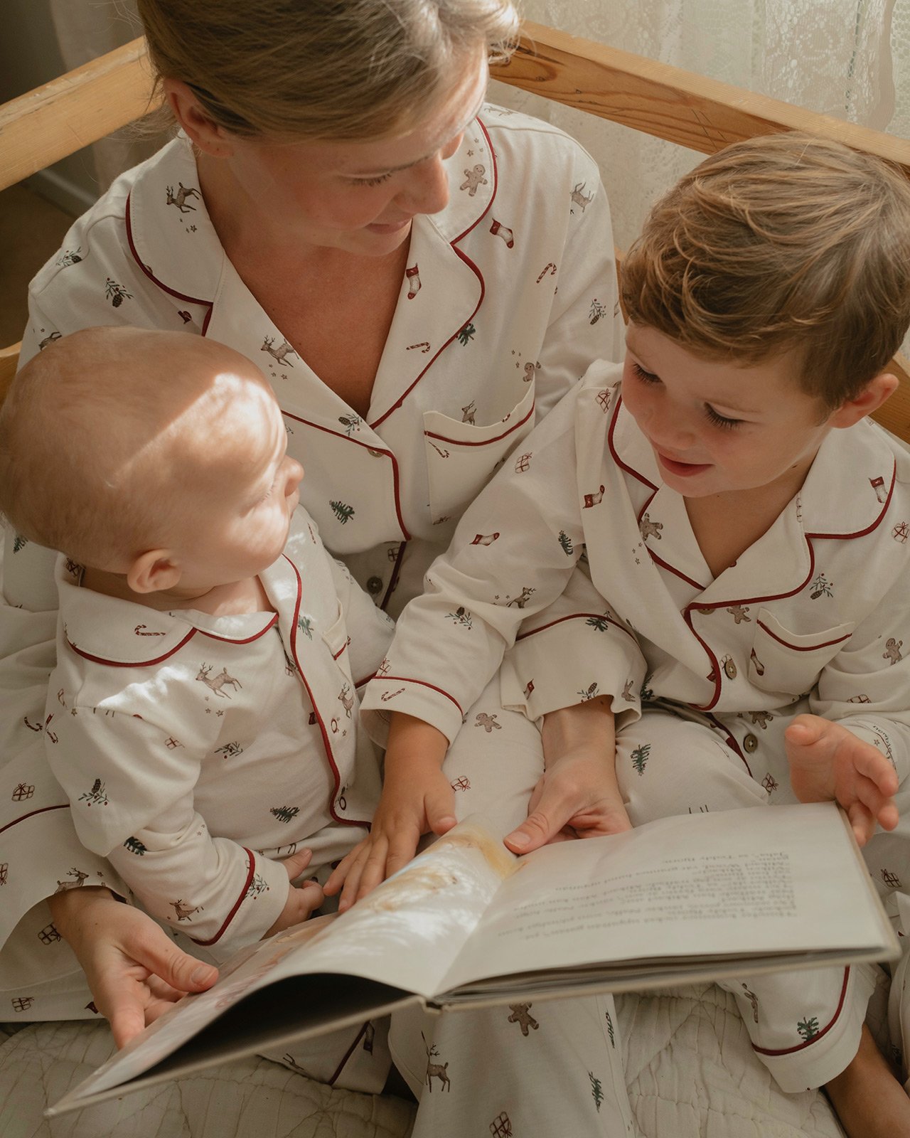 Erwachsene Person und zwei Kinder in passenden Pyjamas mit Festtagsmotiven beim gemeinsamen Lesen