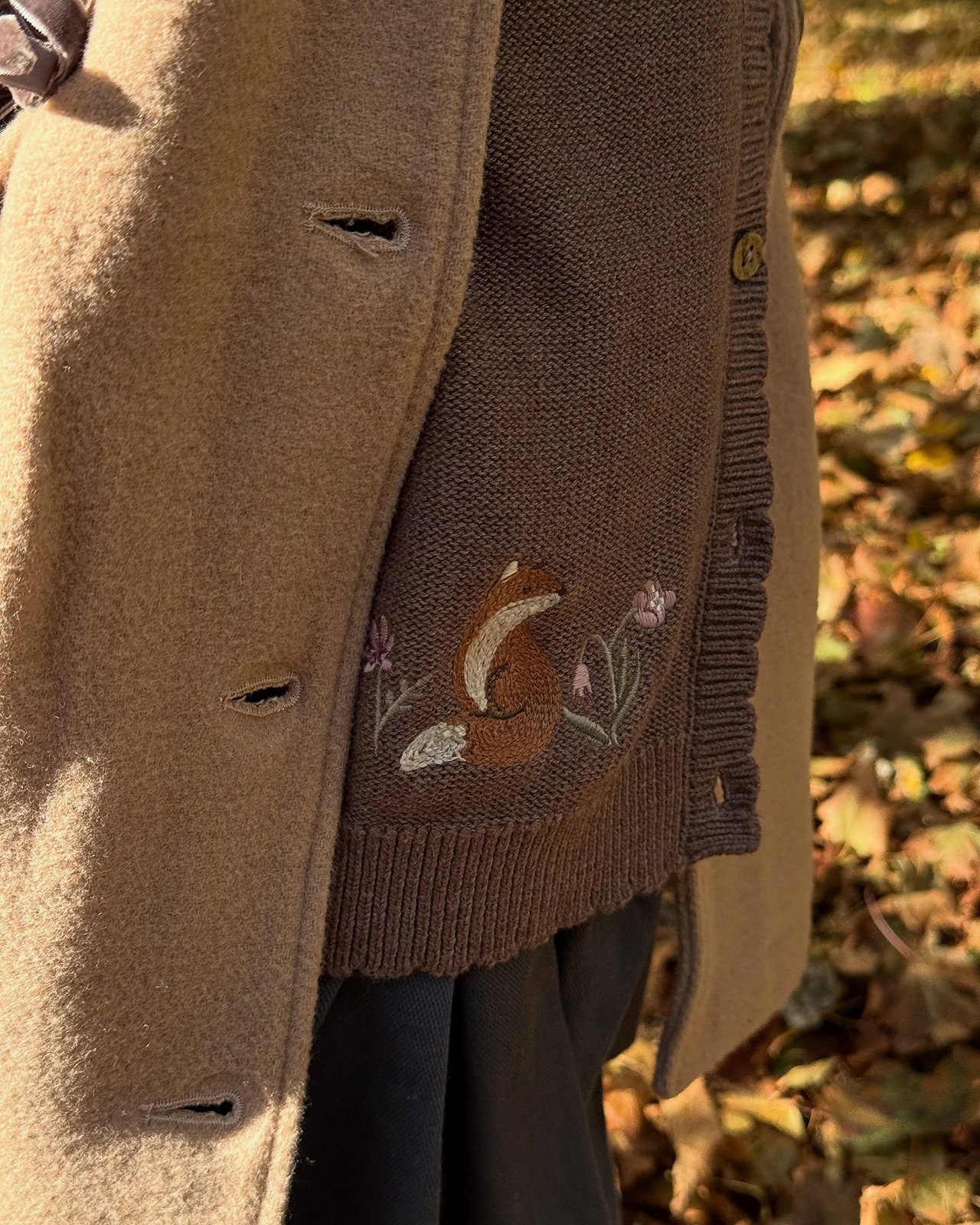 Brown knit cardigan with embroidered fox and flowers, layered under a beige coat