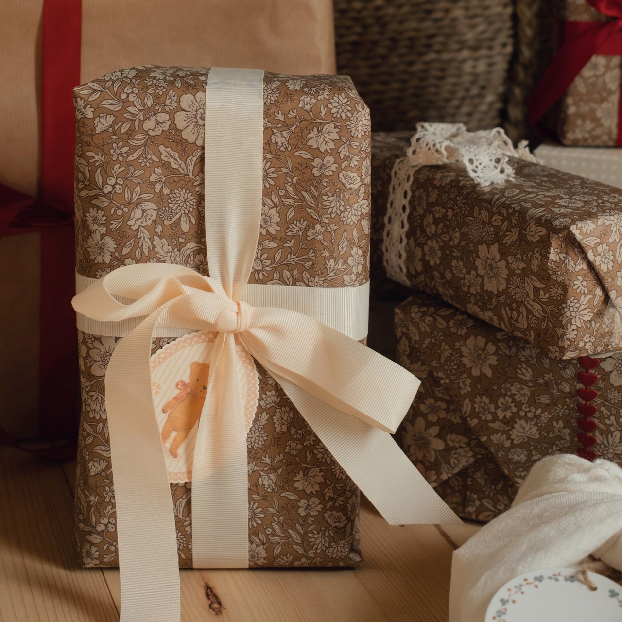 Blumenverpackte Geschenke mit cremefarbenen Bändern, Spitzendetails und einem Teddybär-Geschenkanhänger