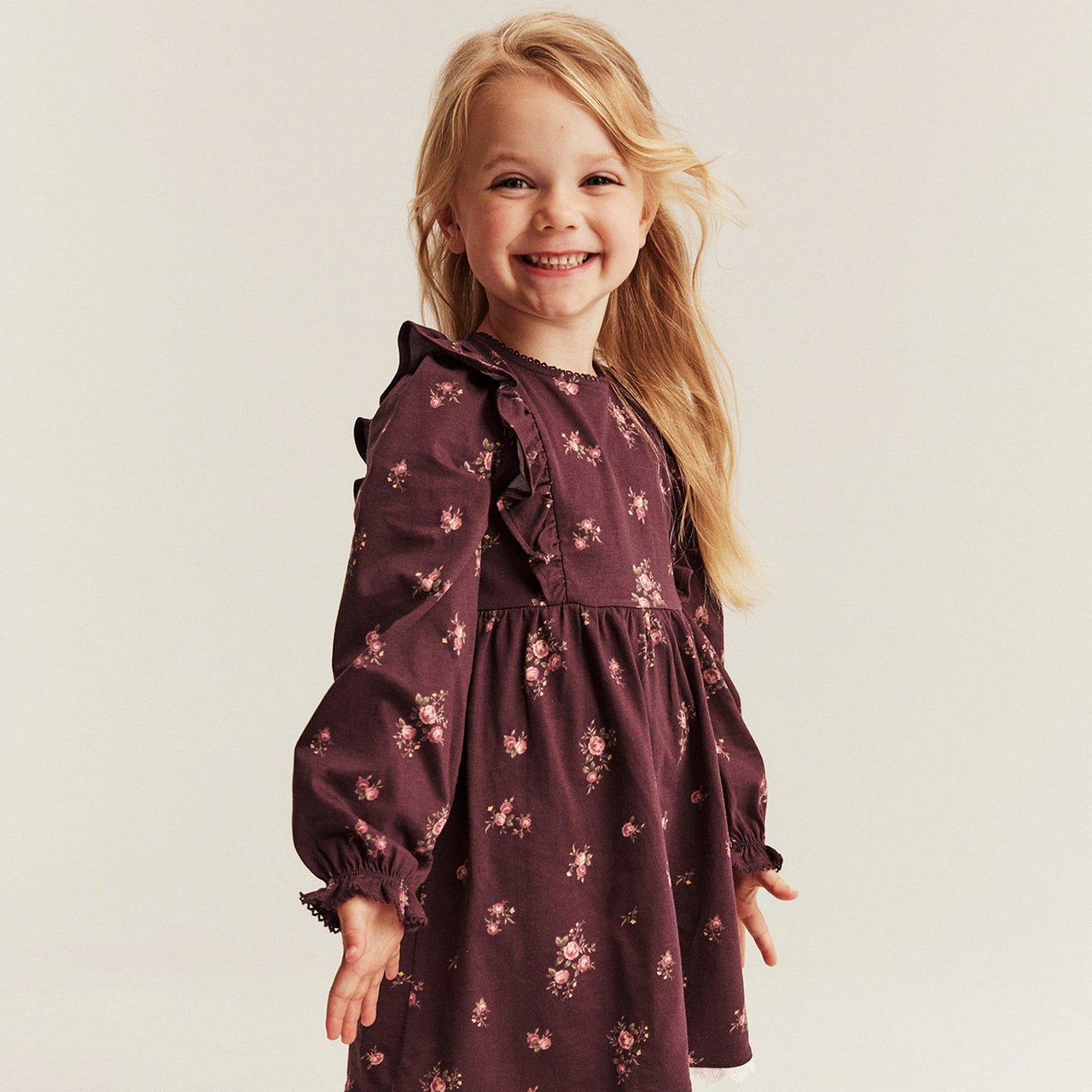 Dark purple long-sleeved dress with floral print, ruffle details and gathered waist for children.