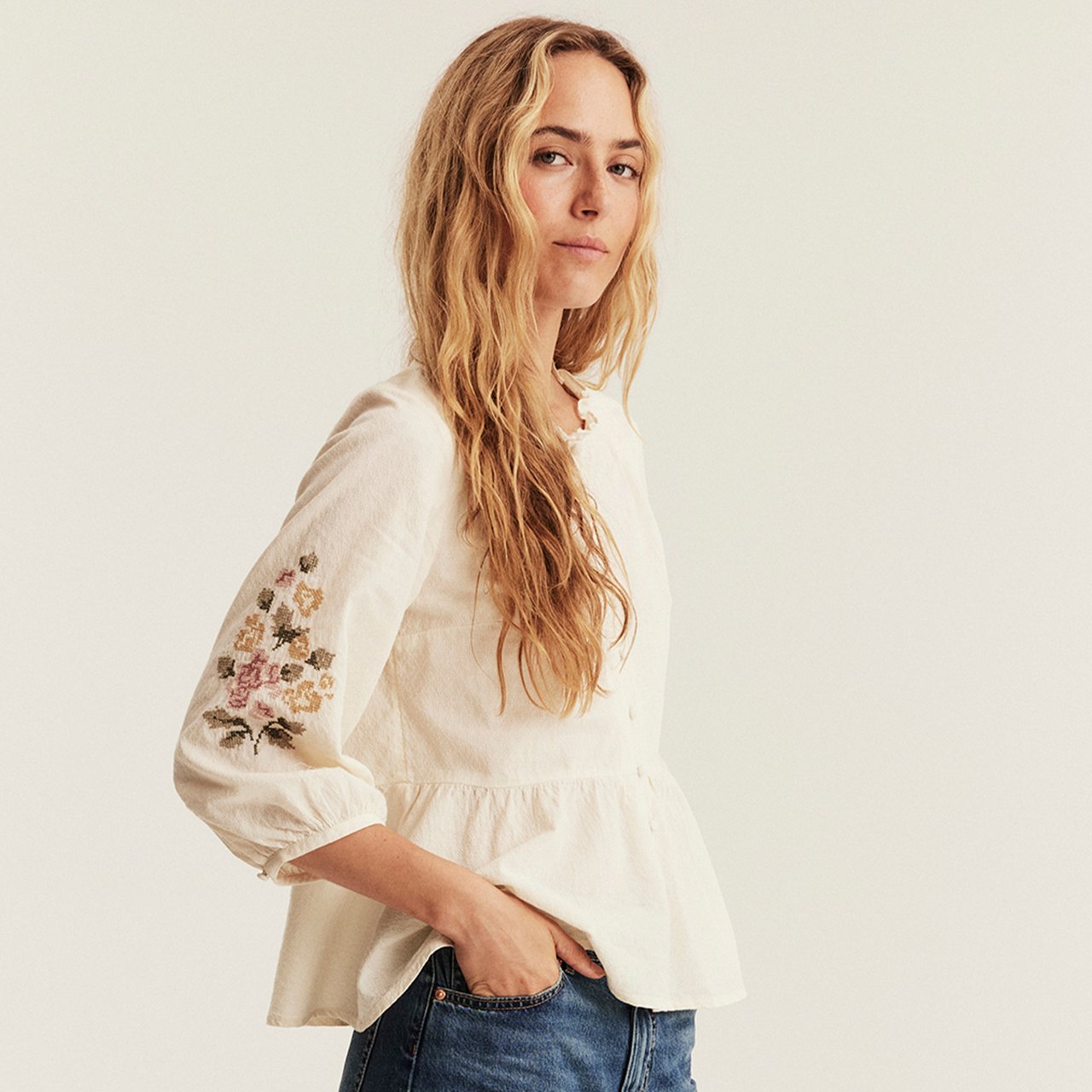 Off-white blouse with floral embroidery on sleeves, three-quarter puff sleeves and a gathered peplum hem.