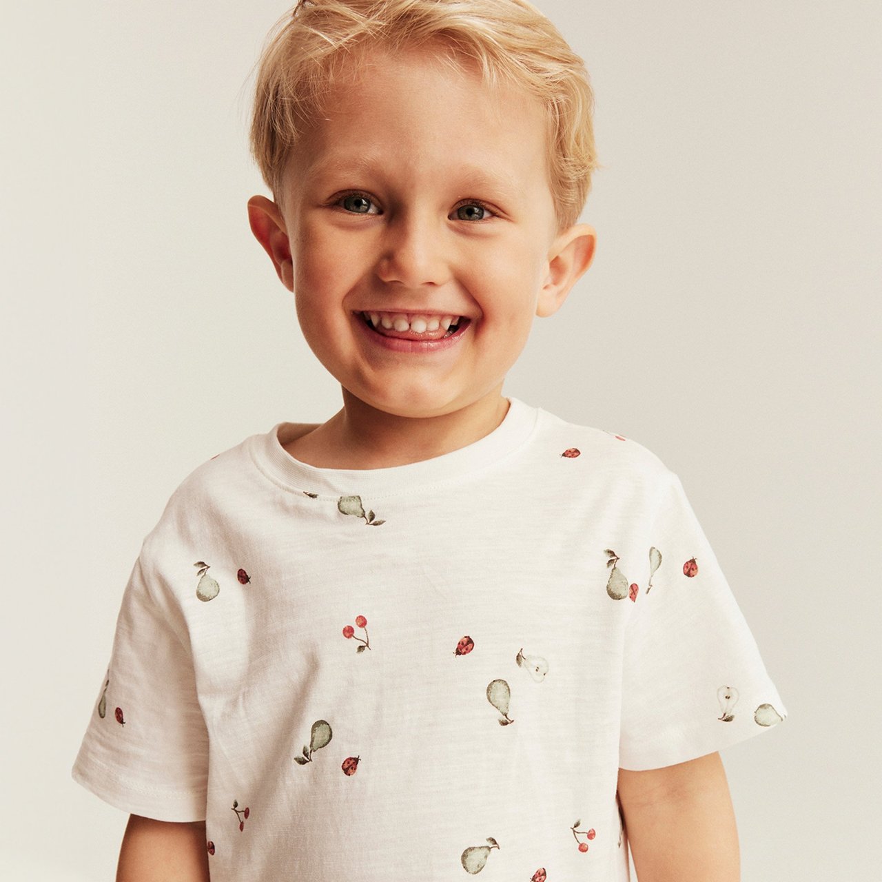 Boy wearing a white short‑sleeve t‑shirt with small print, photographed against a neutral background.