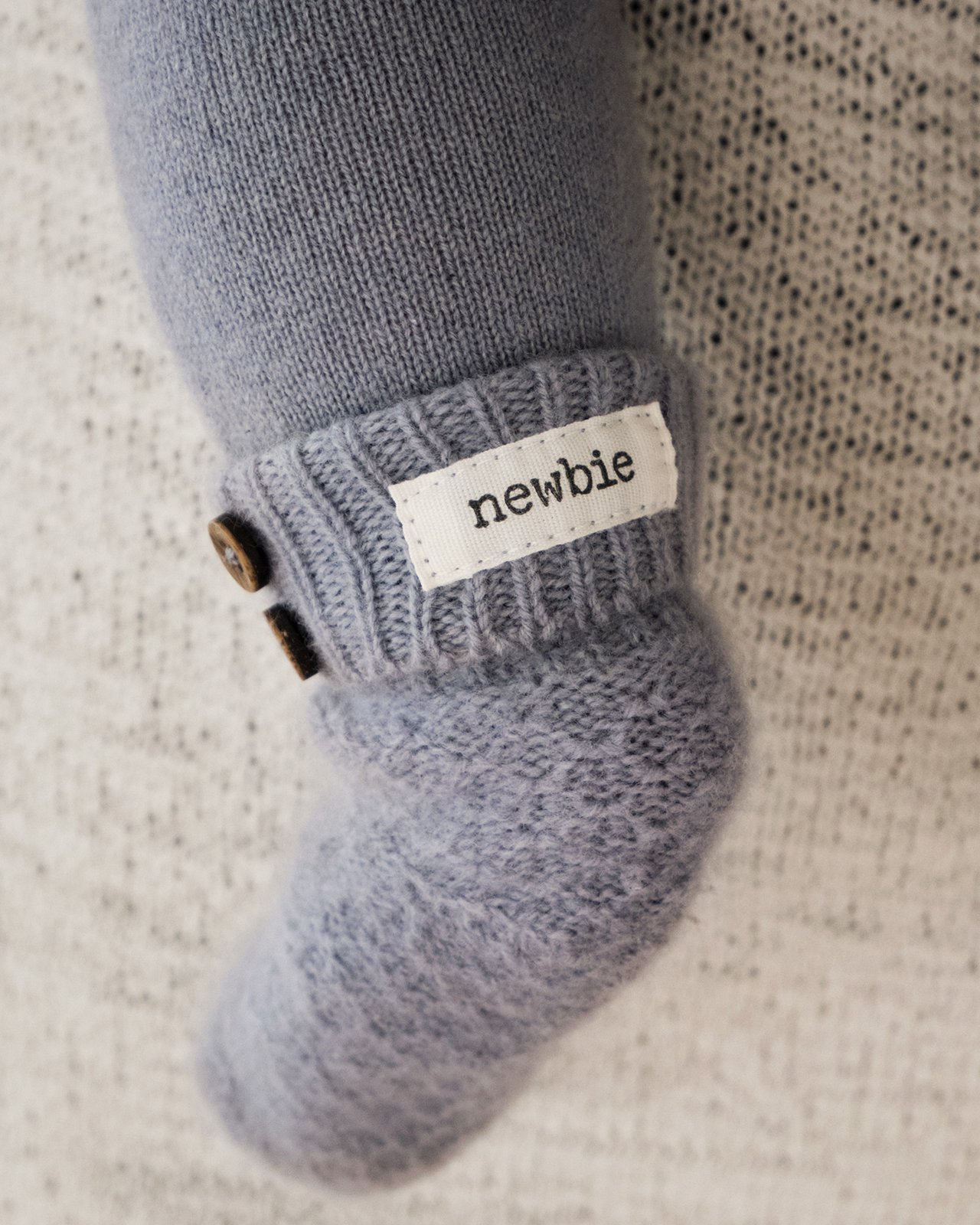 Close-up of a baby’s light blue knitted wool sock with Newbie label from the wool guide