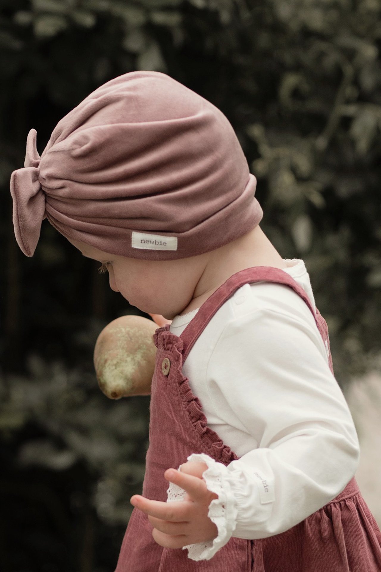 Dusty pink bow hat and corduroy pinafore dress worn with a white long-sleeved top.