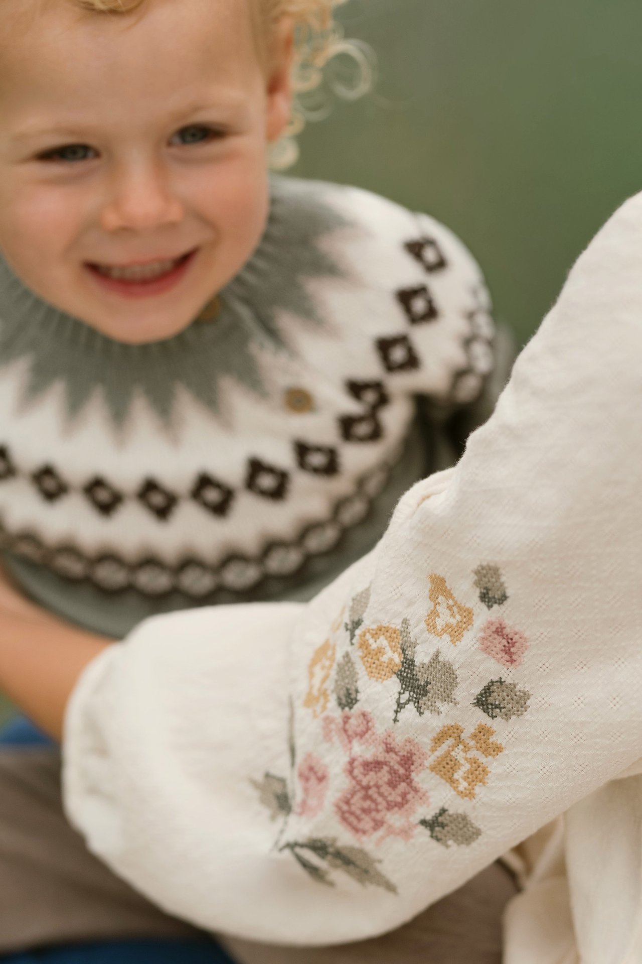 Brown and green teddy fleece jackets with animal motifs hanging on wooden wall hooks.