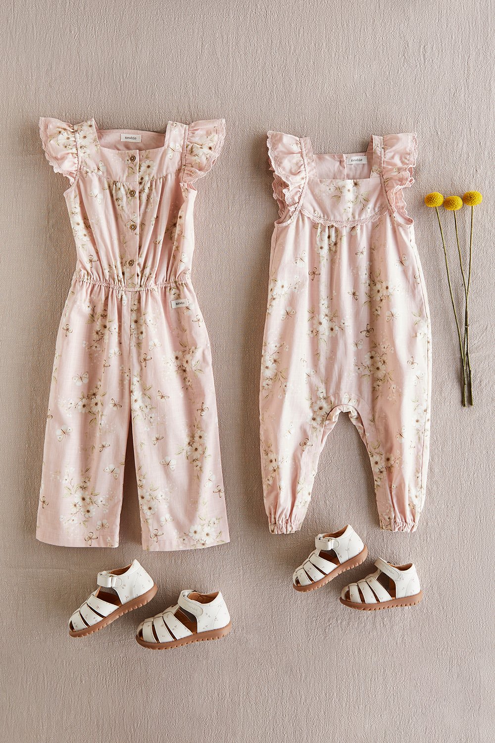 Matching floral baby outfits in soft pink laid flat on a neutral background, with ruffled details and small sandals.