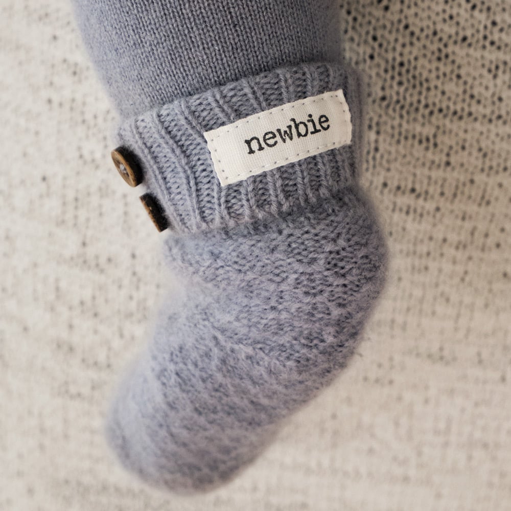 Light blue knitted baby socks with cable-knit pattern, folded ribbed cuff, wooden buttons and Newbie label.