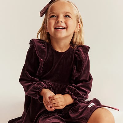 Child wearing a burgundy velvet dress with ruffle details.