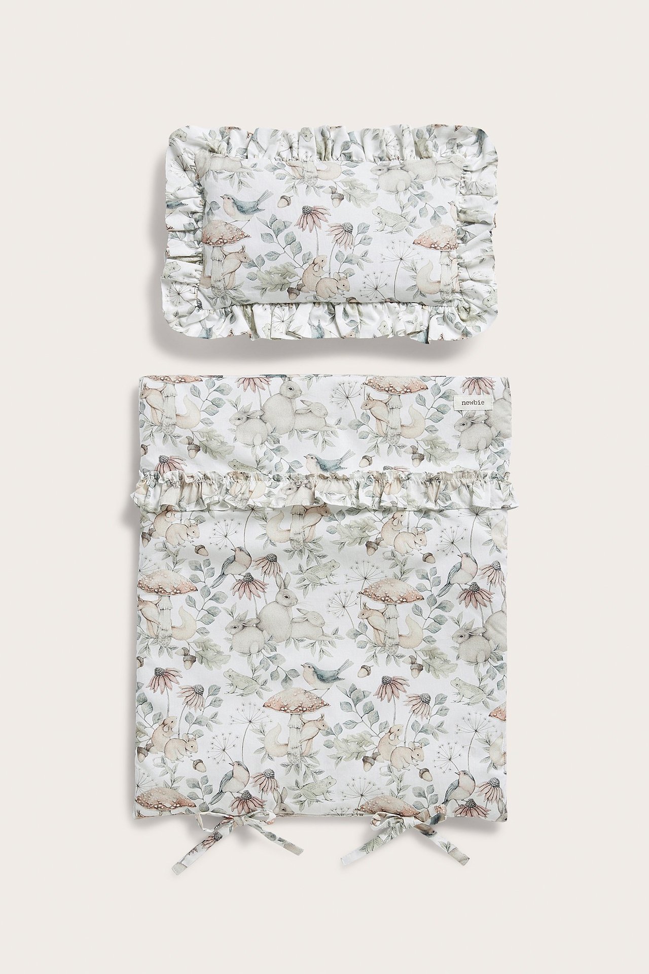 Vorderansicht: Hellbeiges Puppenbett-Bettwäscheset mit Waldtier-Print, Rüschen und Schleifen.