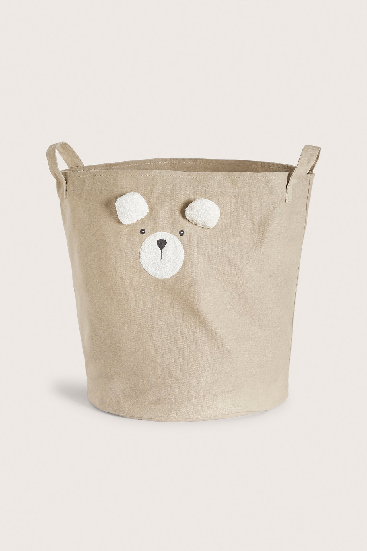 Front view of a beige cotton storage basket with a bear face, embroidered nose, and fluffy pile ears.