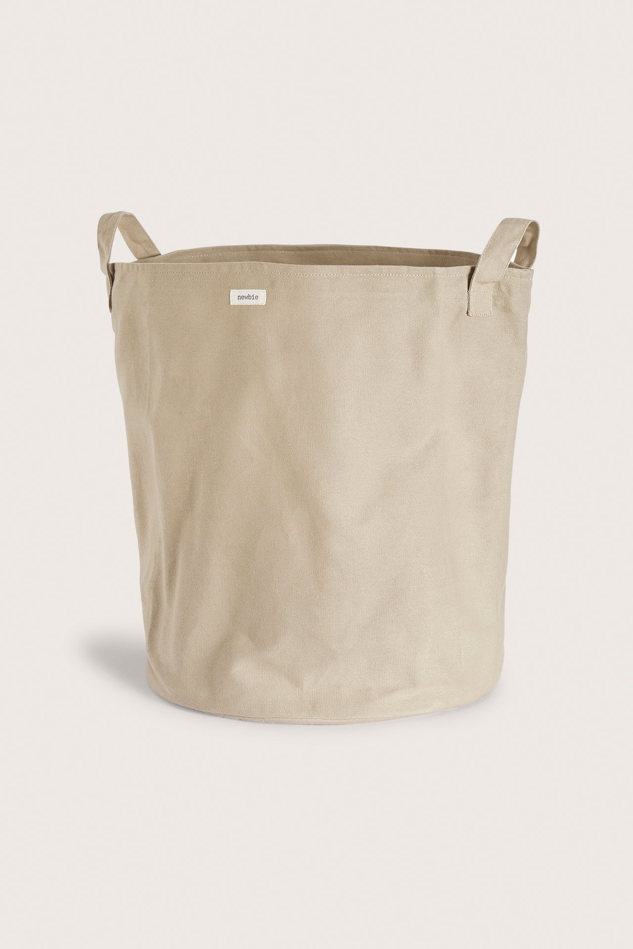 Front view of a beige cylindrical cotton storage basket with two fabric handles and a small label.