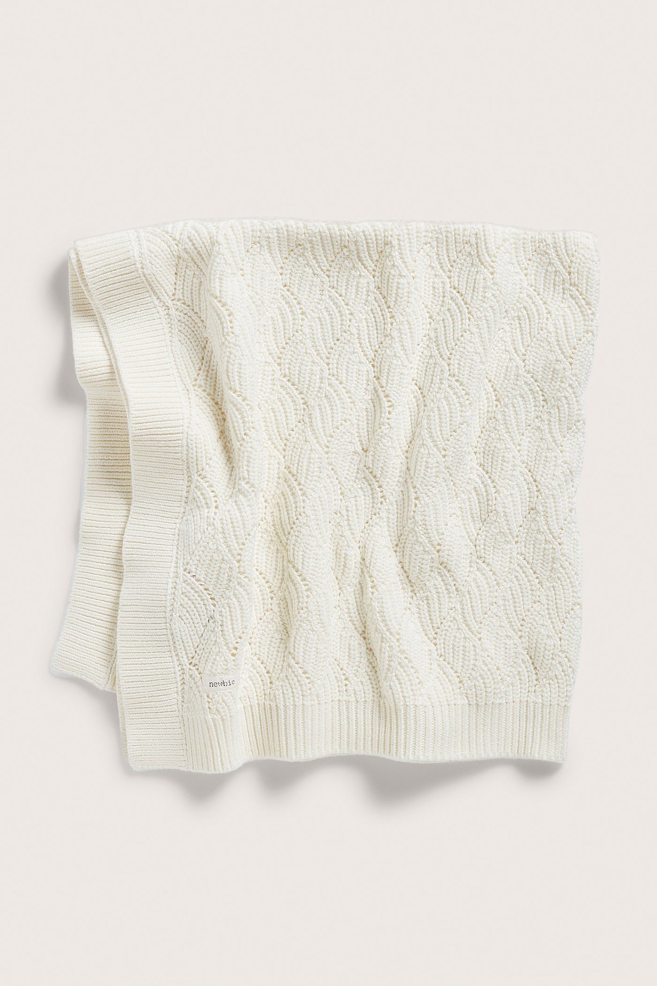 Top view of an off-white knitted cotton baby blanket with a jacquard pattern and ribbed edges.