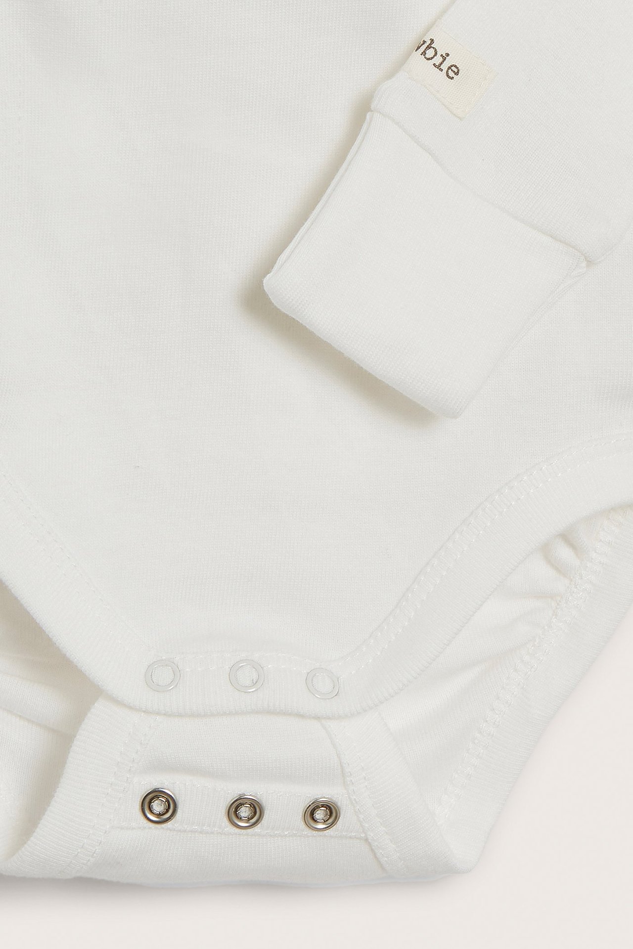 Close-up of an off-white long-sleeved baby wrap-around bodysuit with snap buttons at the crotch.