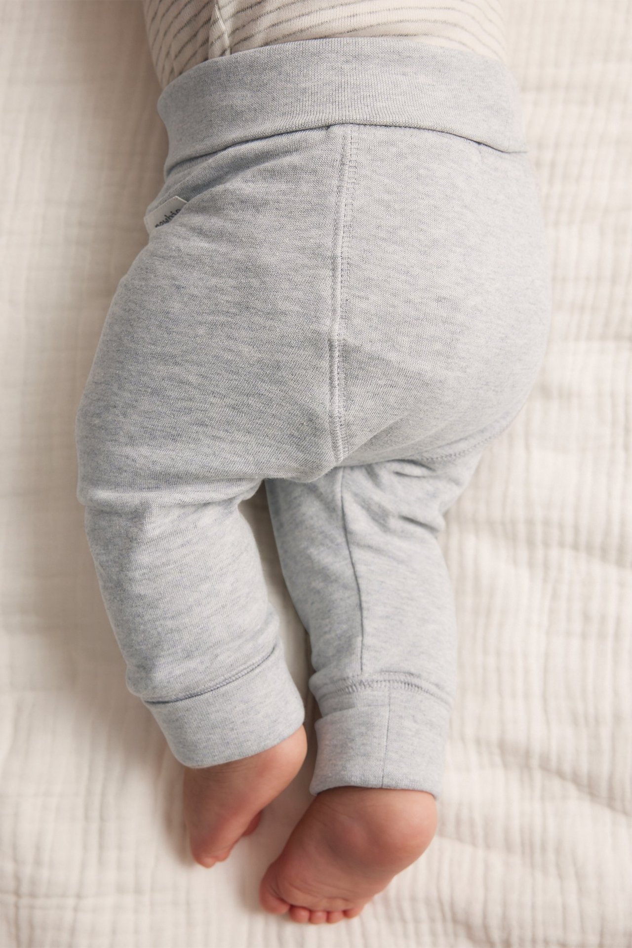 Close-up of a baby wearing grey melange cotton leggings with a wide waistband and folded cuffs.