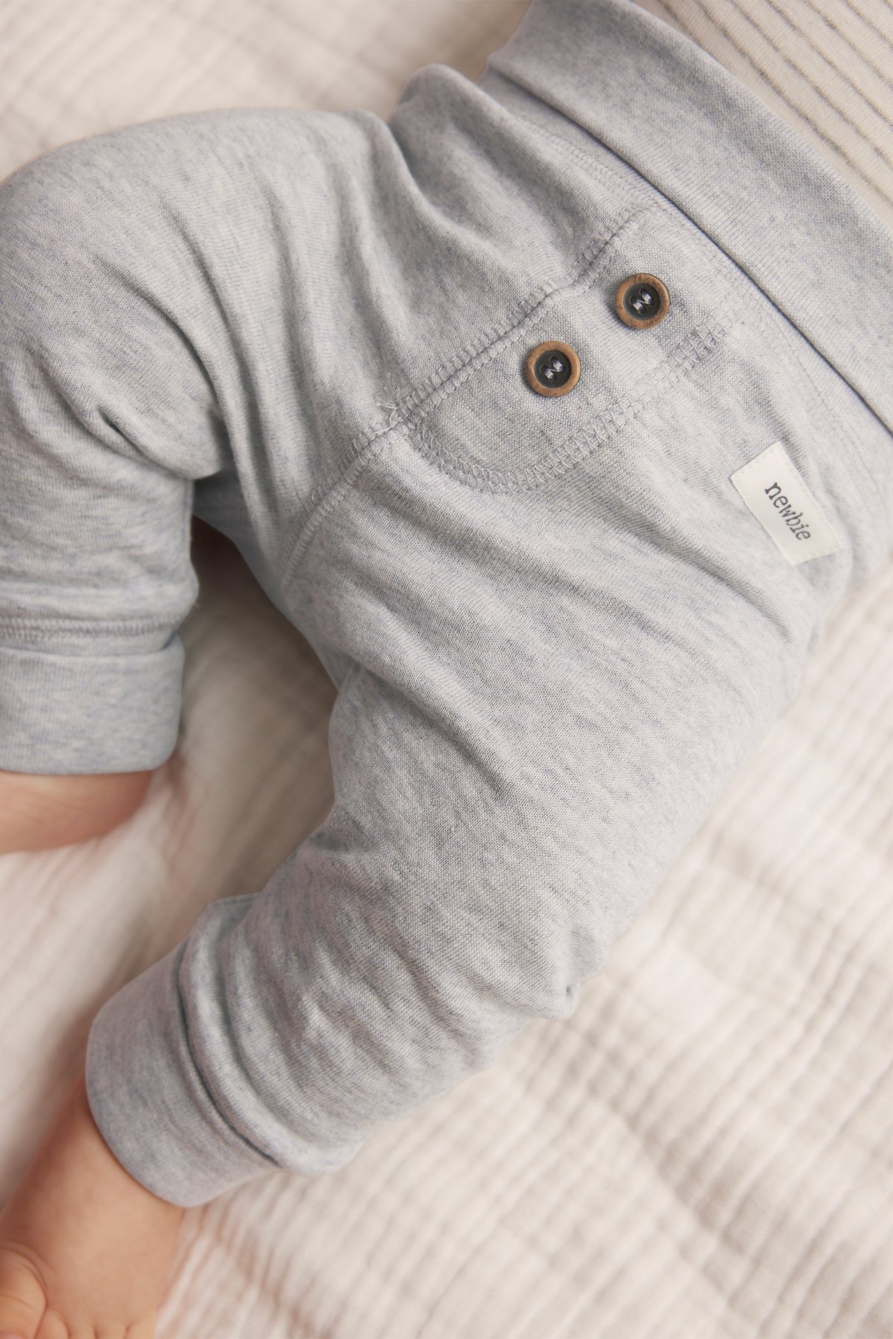 Close-up of baby wearing grey melange cotton leggings with a fold-down waist and decorative buttons.