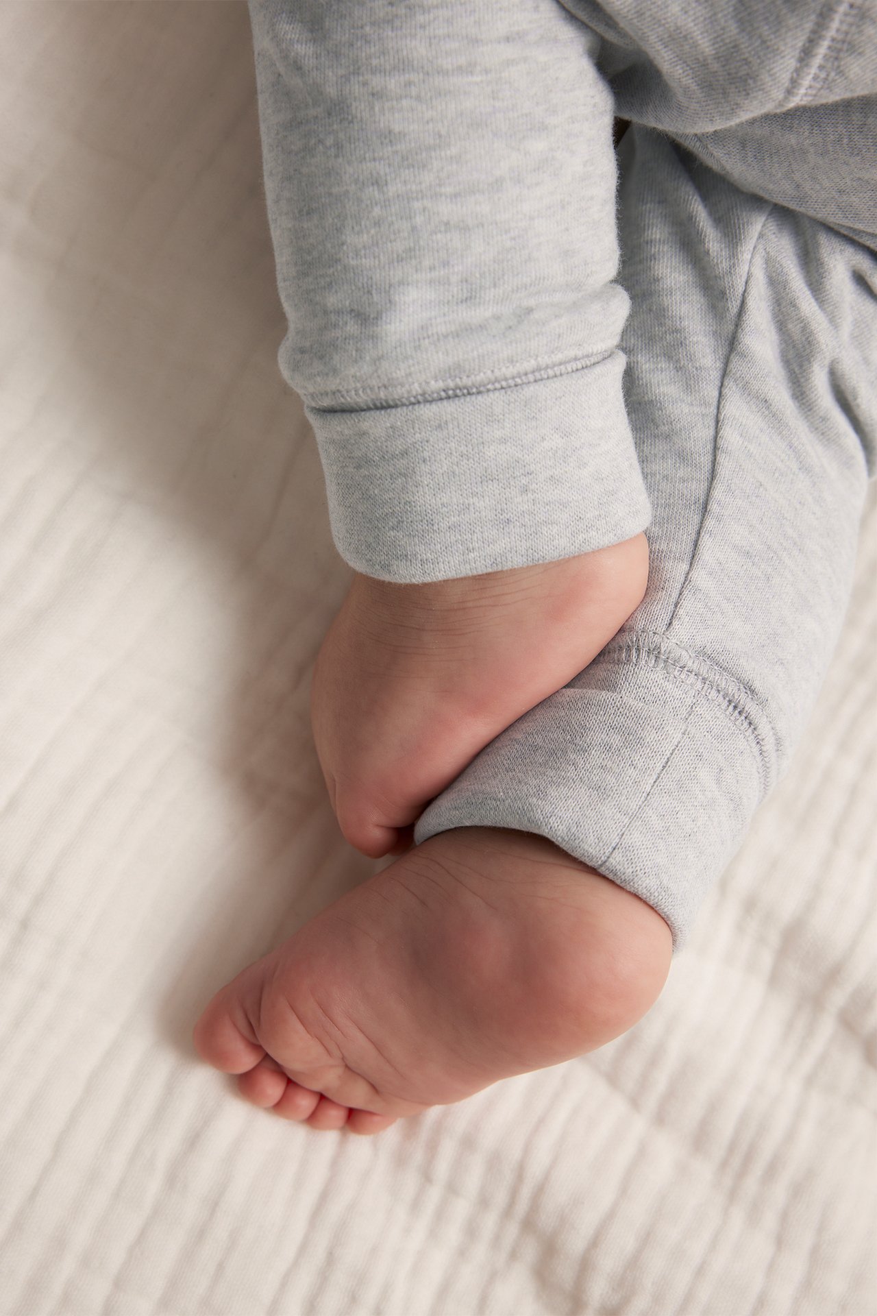 Close-up of a baby wearing grey melange cotton leggings with folded cuffs, showing bare feet.
