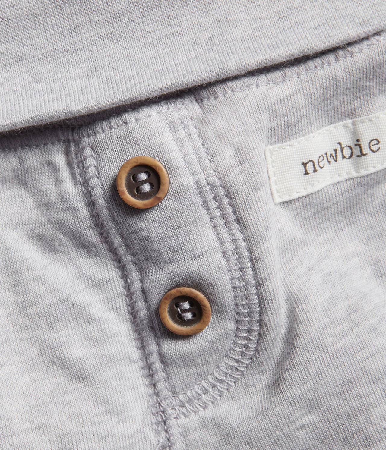 Close-up of grey melange baby cotton leggings with two decorative brown buttons and a white label.