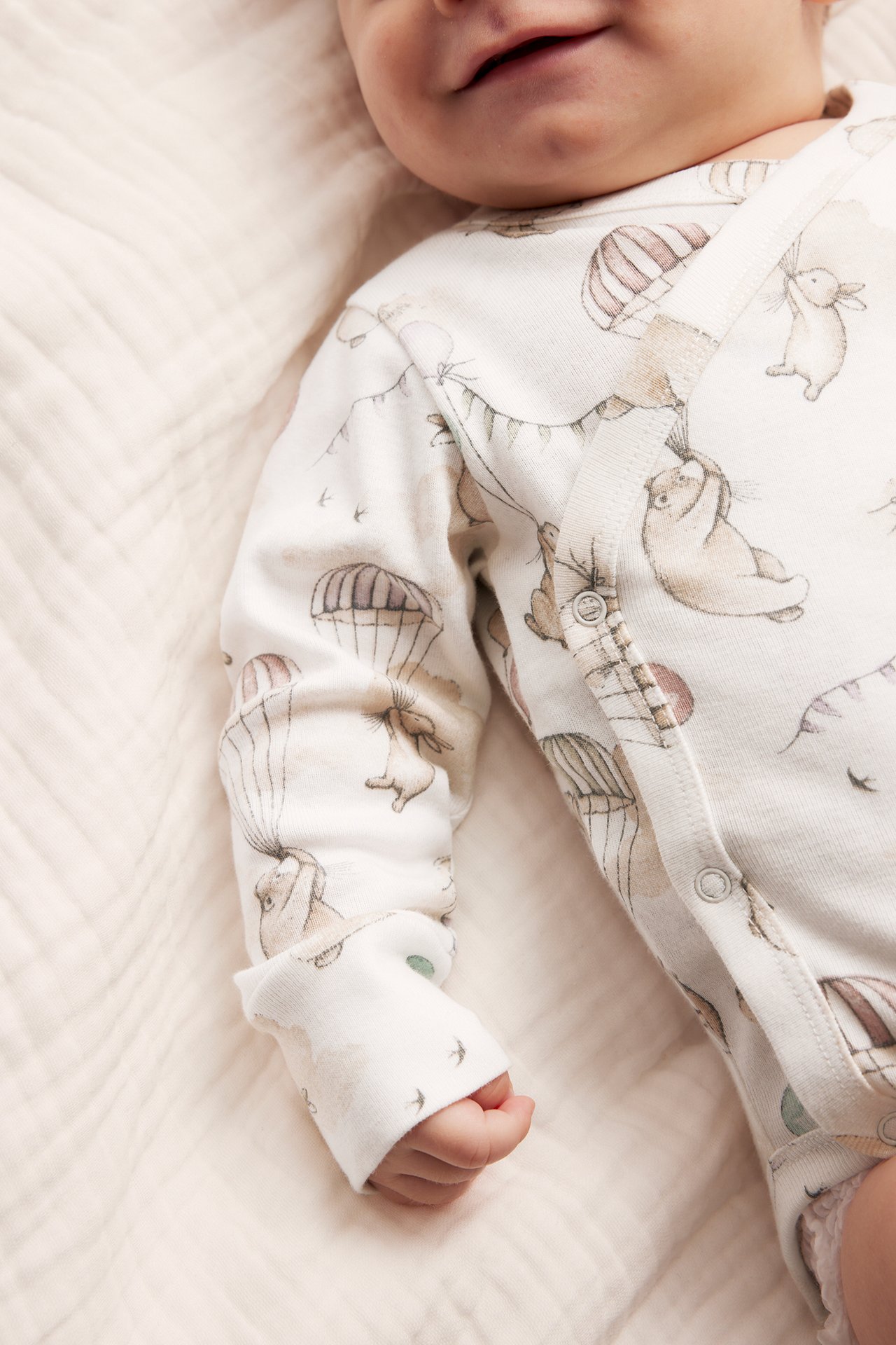 Close-up of a baby wearing an offwhite patterned wrap bodysuit with long sleeves and popper buttons.