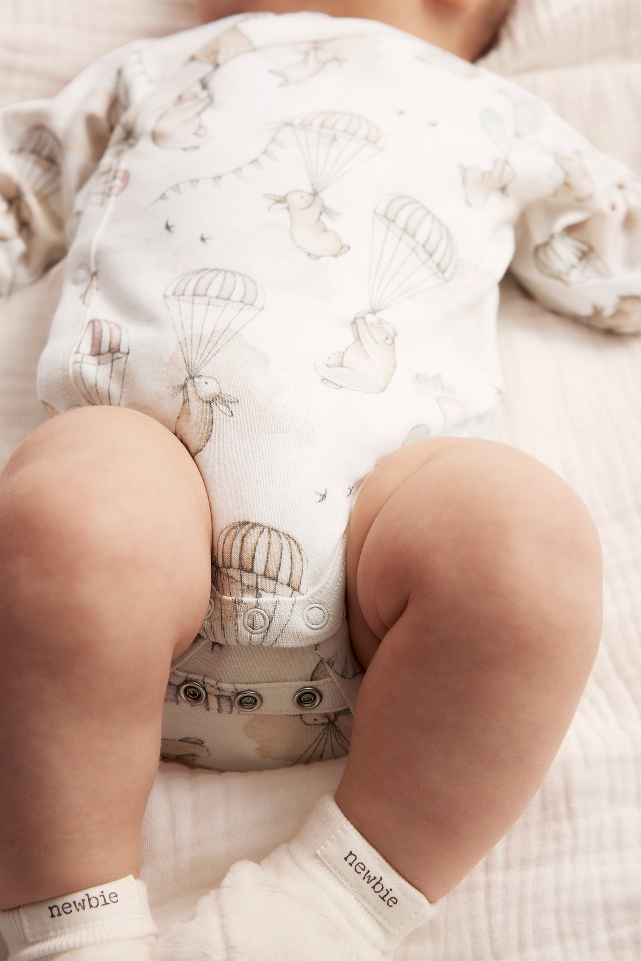 Top-down view of a baby wearing an off-white patterned wrap bodysuit with parachuting animals and white socks.
