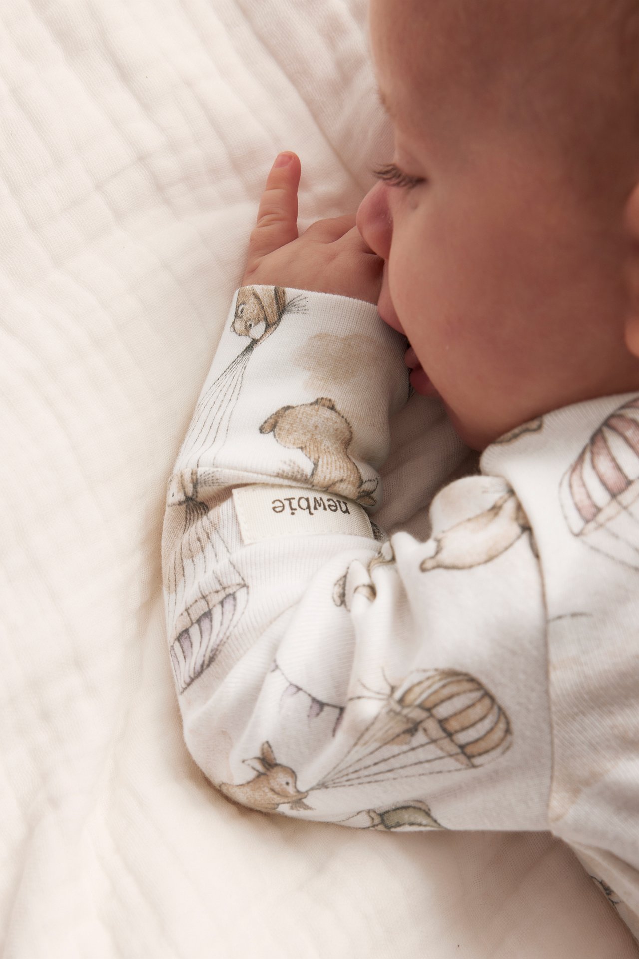 Close-up of baby in off-white patterned long-sleeved wrap bodysuit with animal and balloon motifs.