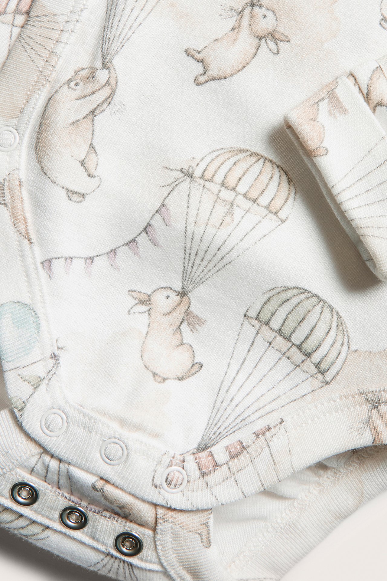 Close-up of an off-white baby wrap bodysuit with rabbit, bear, and balloon parachute print, featuring snap buttons.