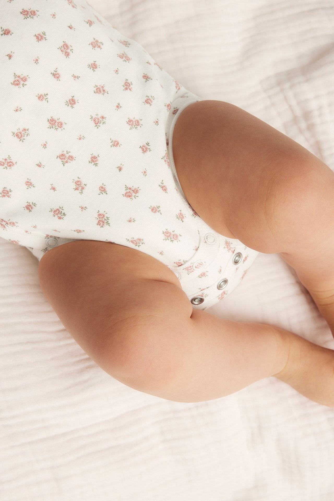 Close-up of a baby wearing an off-white cotton bodysuit with a pink floral pattern and snap buttons.