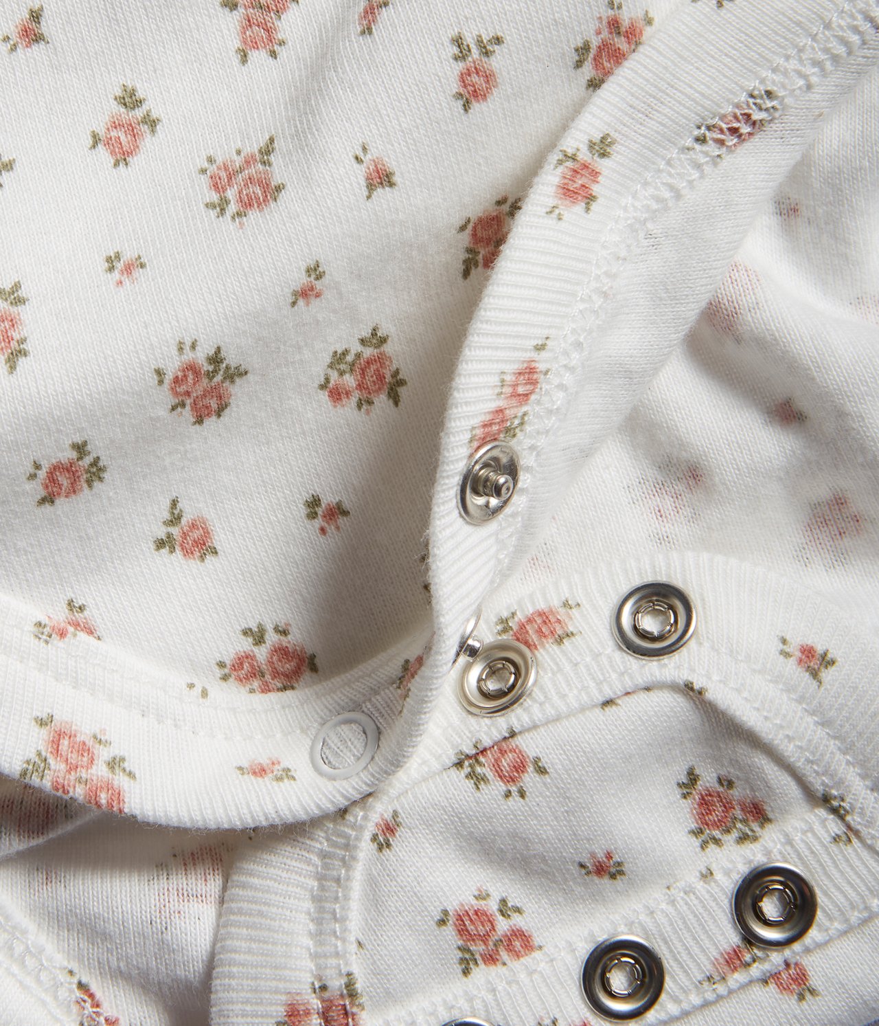 Close-up of an off-white cotton baby bodysuit with a pink floral pattern and snap buttons.