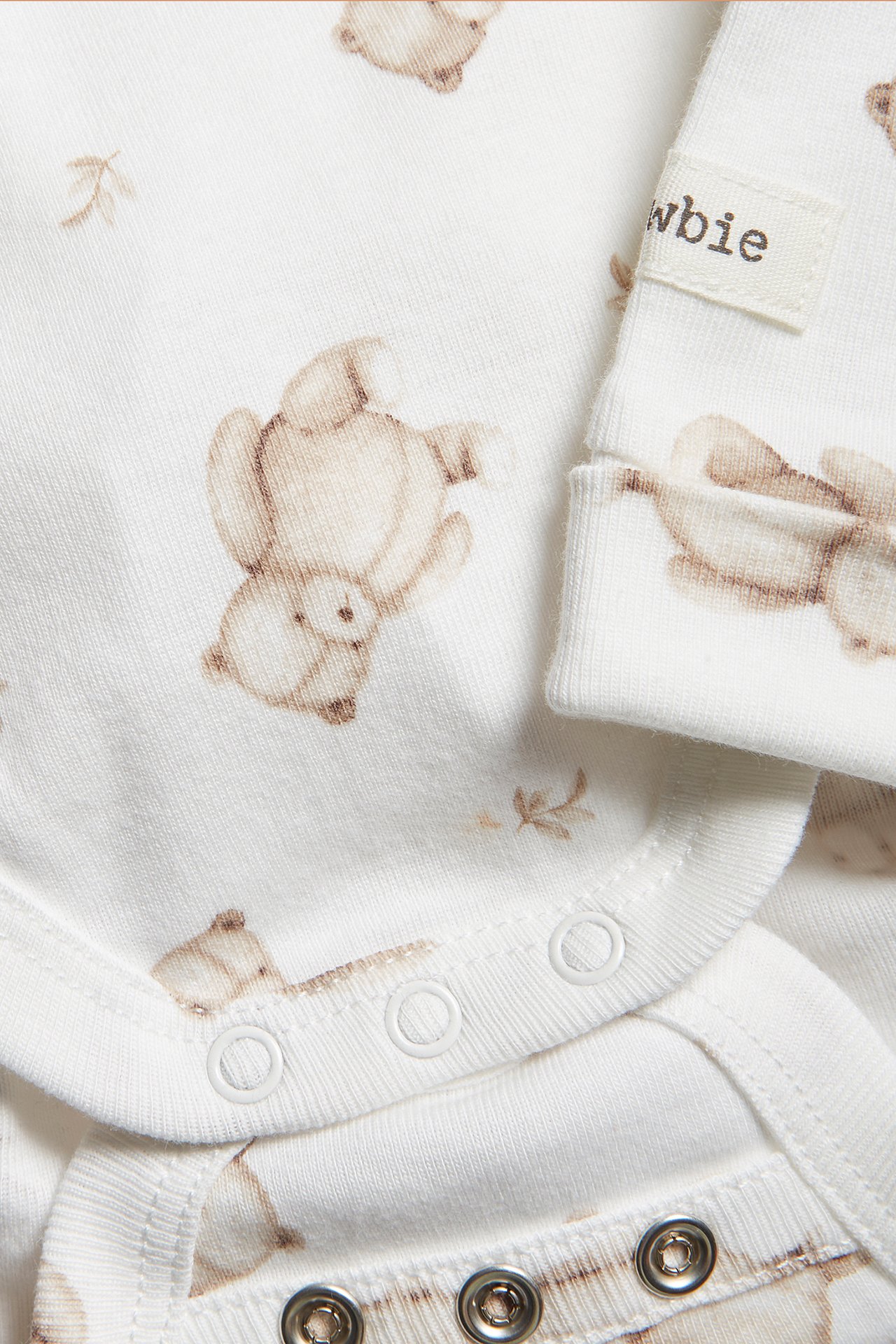 Nahaufnahme eines cremefarbenen Baby-Baumwollbodys mit braunem Teddybärenmuster und Druckknöpfen.