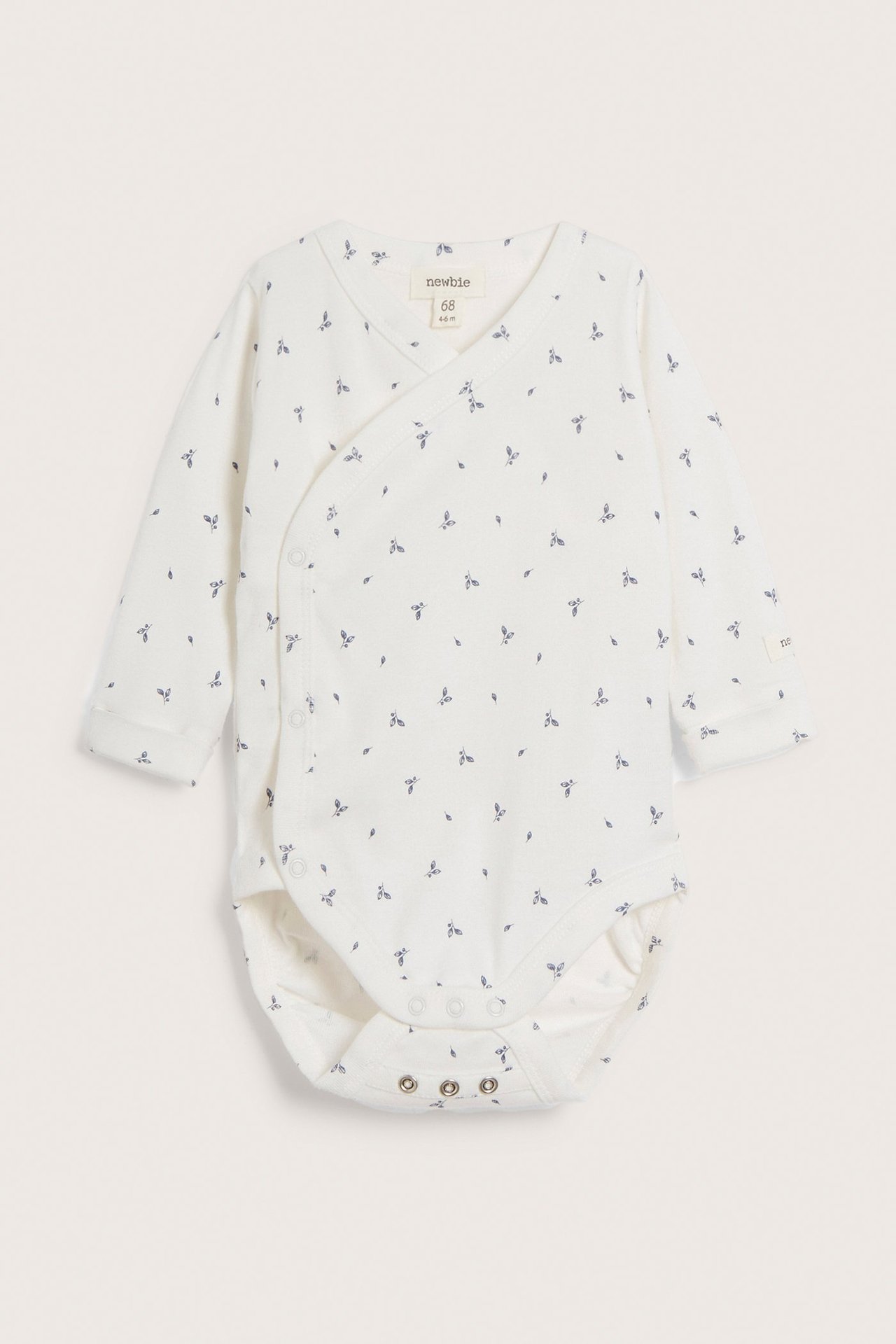 Vorderansicht: Cremefarbener gerippter Baby-Wickelbody mit kleinem blauem Blattmuster und Druckknöpfen.