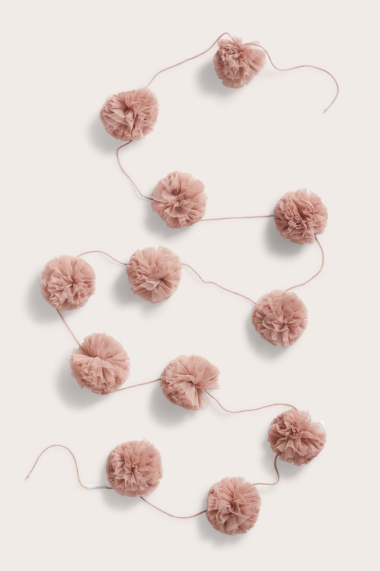 Draufsicht auf eine hellrosa Tüll-Pompom-Girlande mit 12 flauschigen Kugeln auf hellem Hintergrund.
