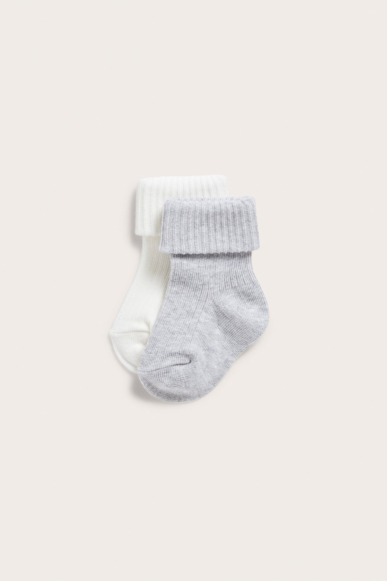 Close-up of two baby ribbed socks, one off-white and one light grey, with folded cuffs.