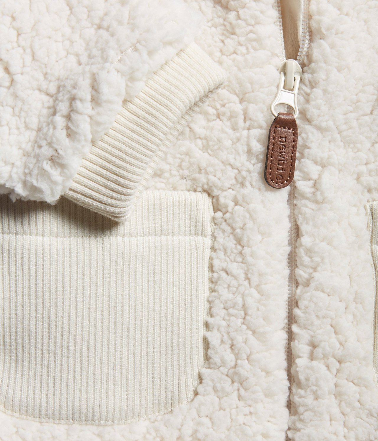 Close-up of a white teddy fur jacket with ribbed cuffs, a ribbed pocket, and a white zipper.