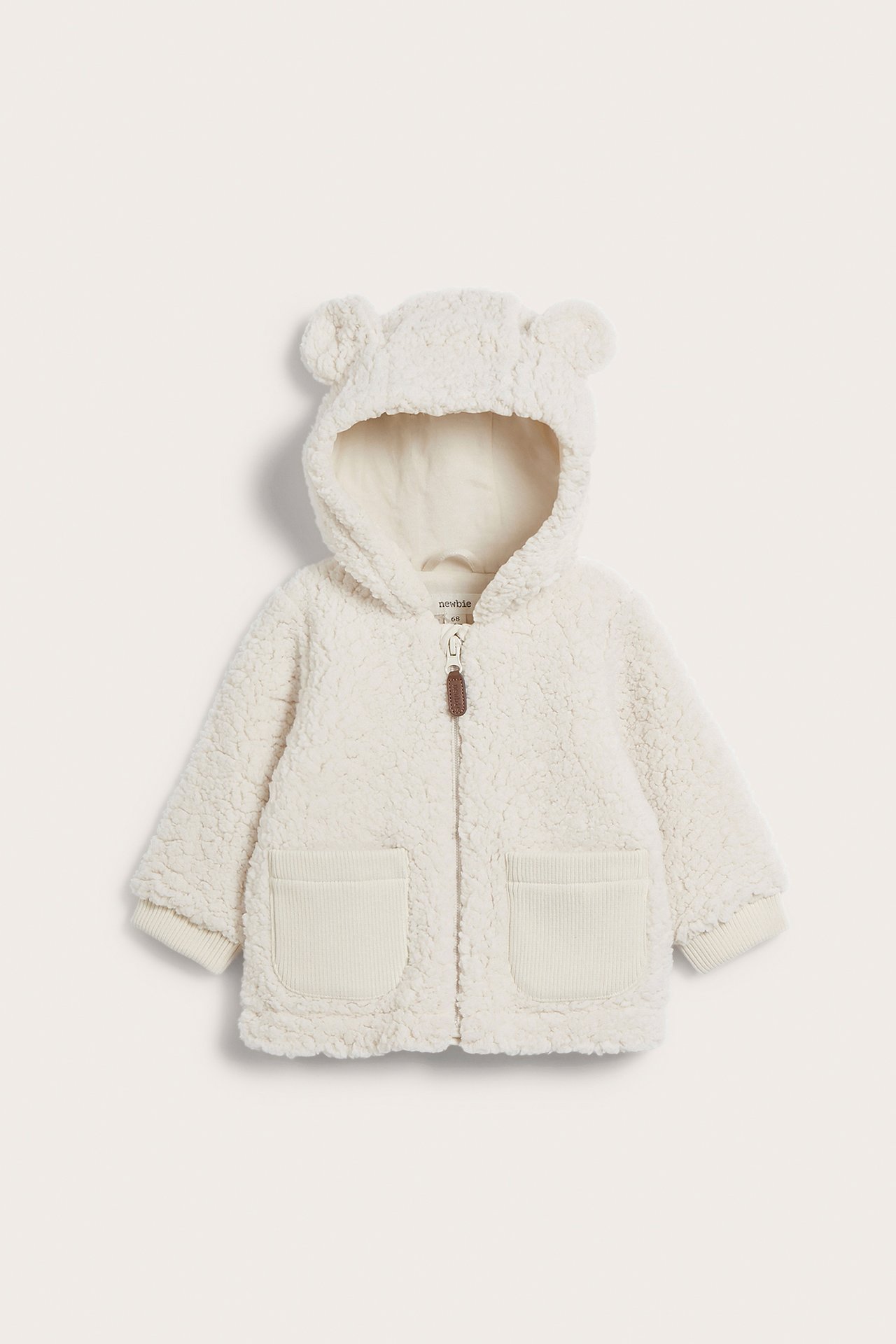 Front view of a white baby teddy fleece jacket with bear ear hood, front zipper, and ribbed pockets.
