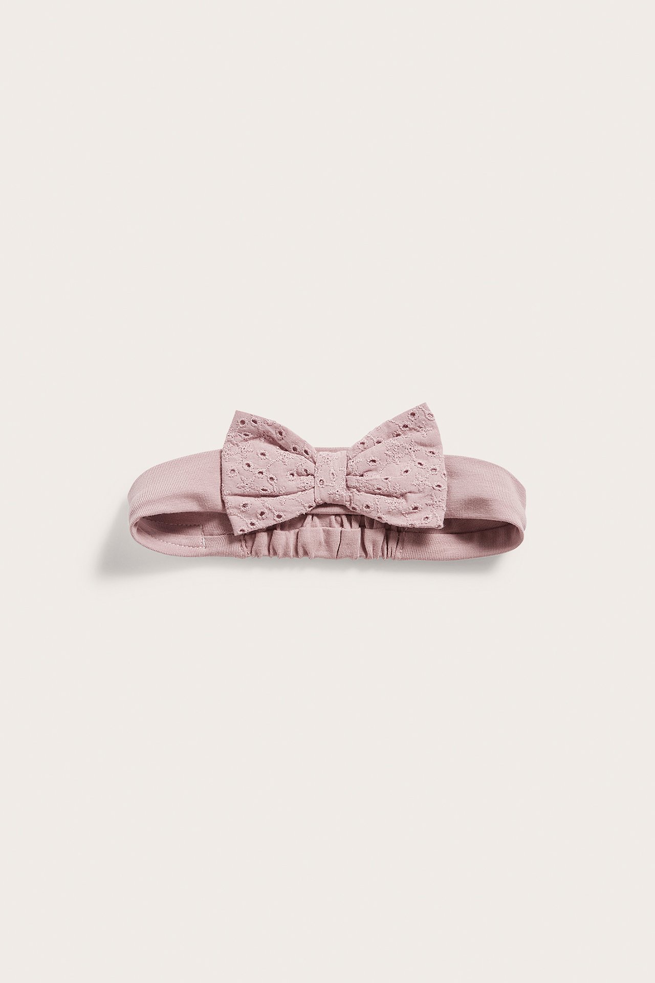Front view of a dusty pink baby headband with an eyelet embroidered bow.