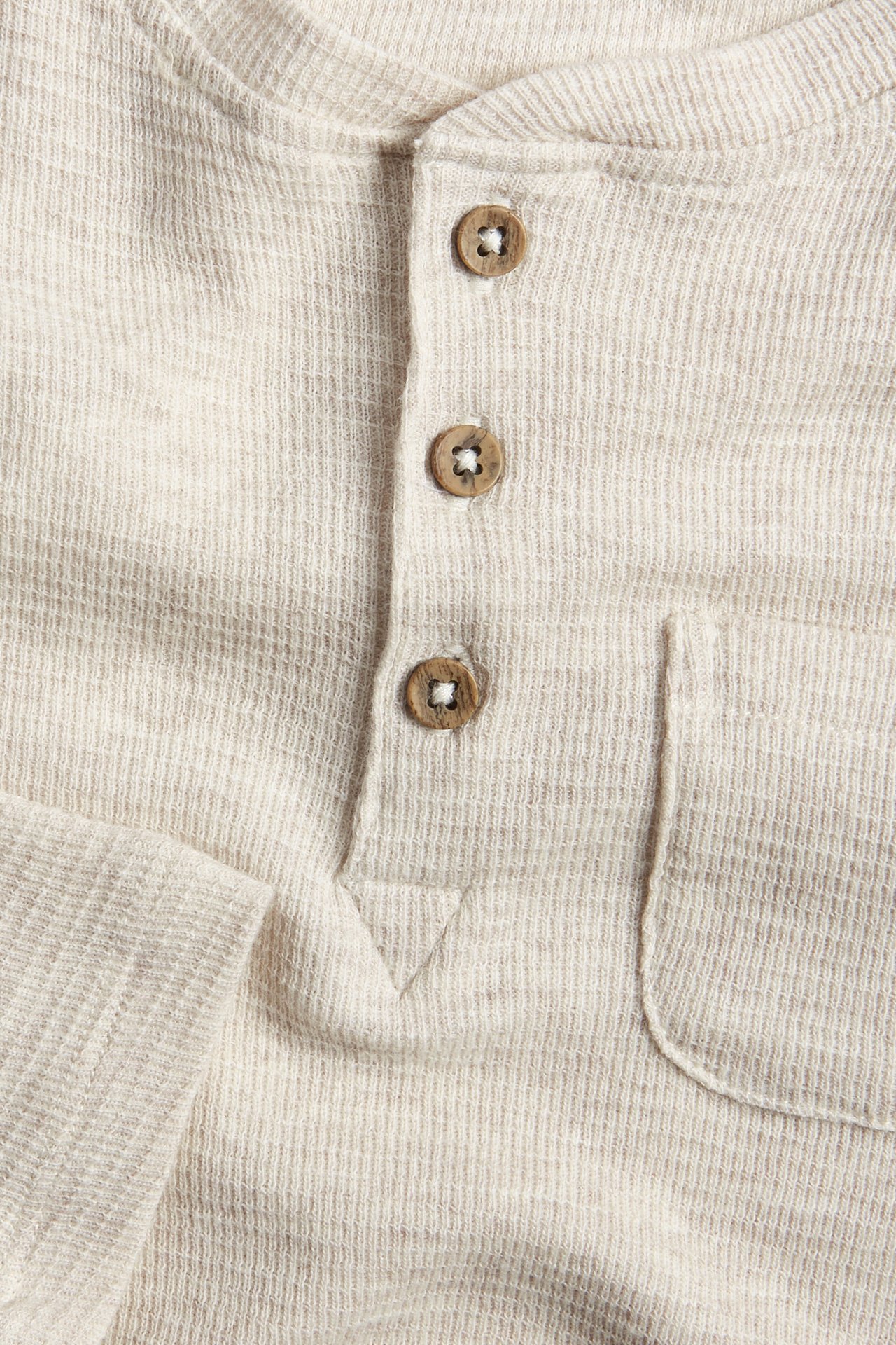 Close-up: Light beige waffle knit henley shirt with three wooden buttons and a chest pocket.