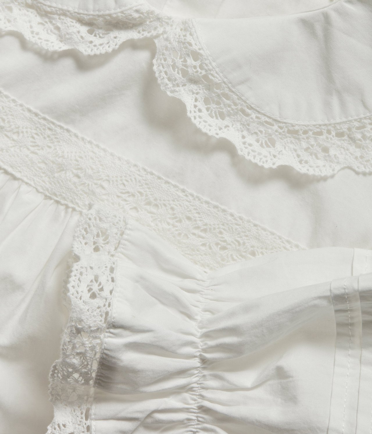 Close-up of an off-white cotton Lucia gown with a lace-decorated rounded collar and gathered details.