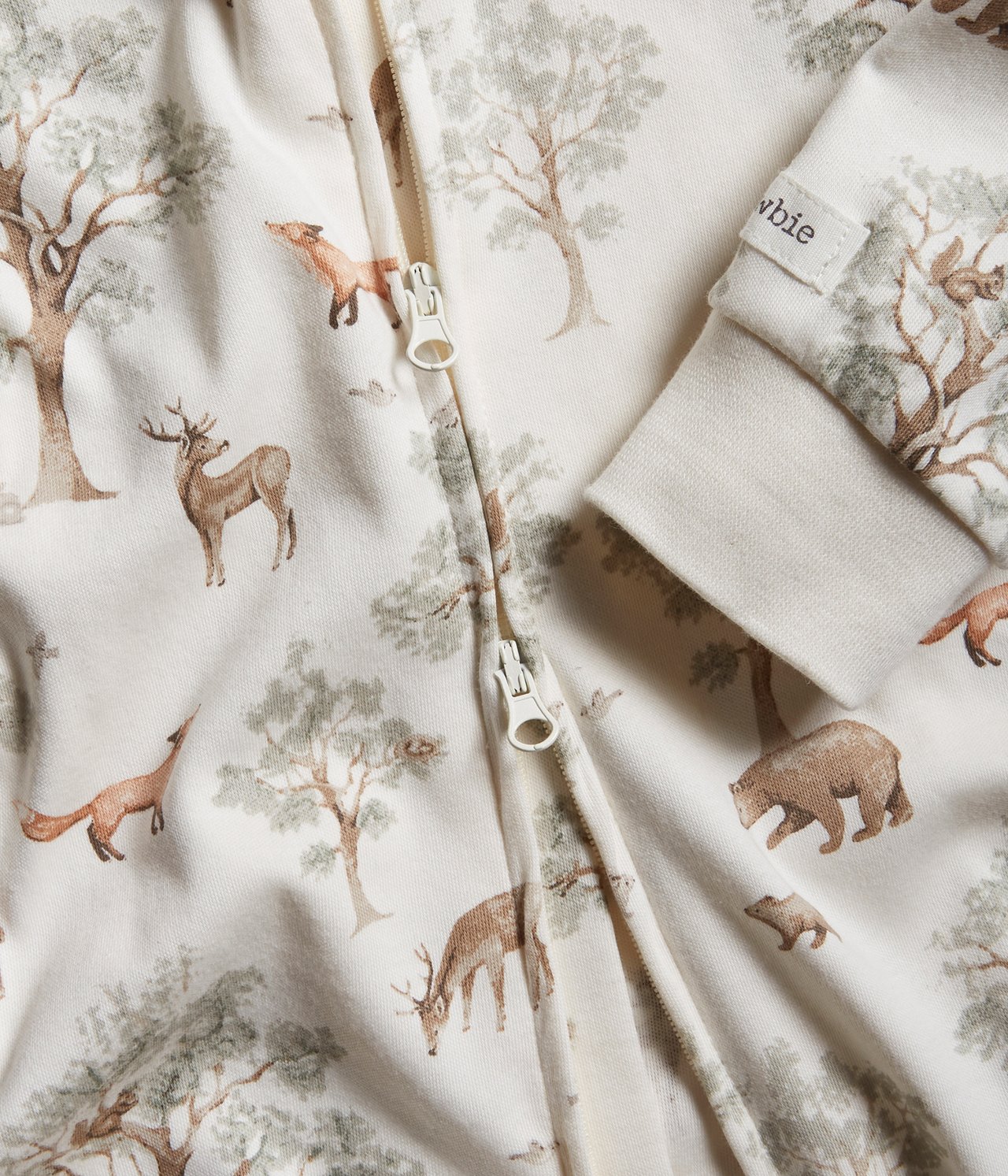 Close-up of an off-white baby cotton pyjamas with a forest print and a two-way front zipper.