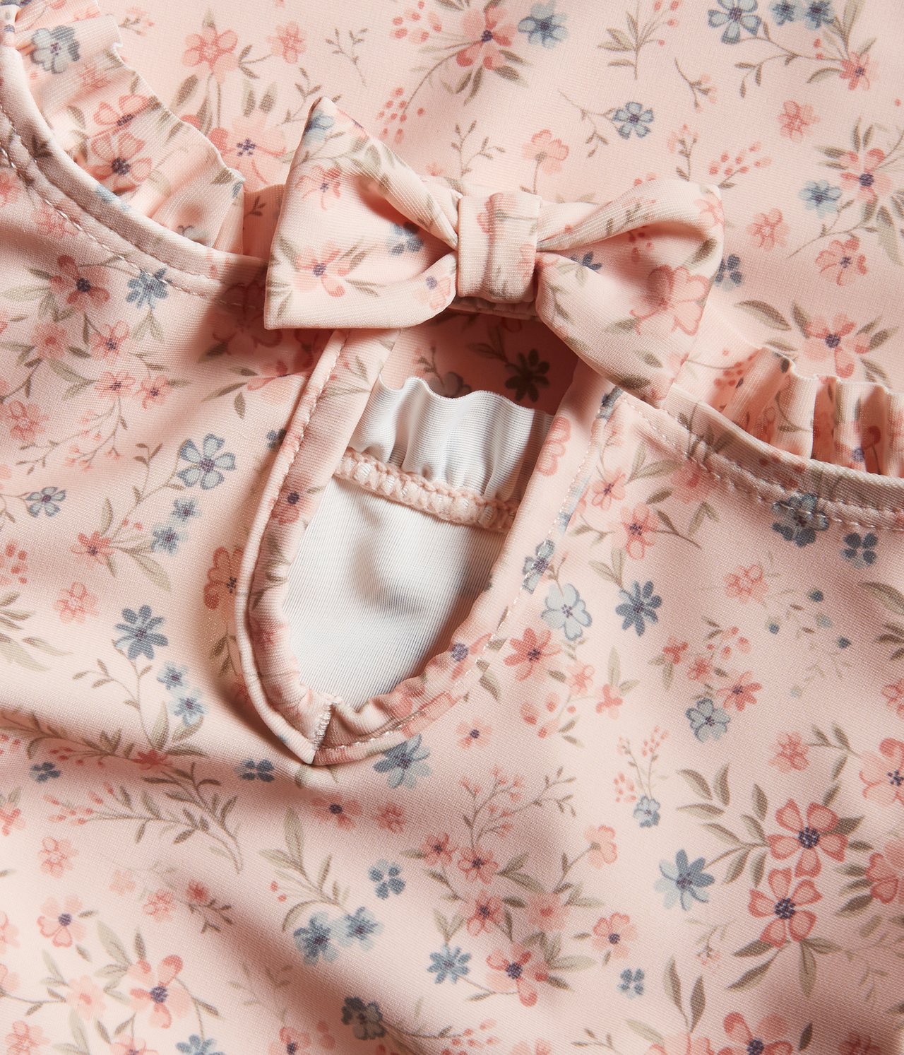 Close-up of a baby/kid's light pink floral UV top with frills and a bow at the neckline.
