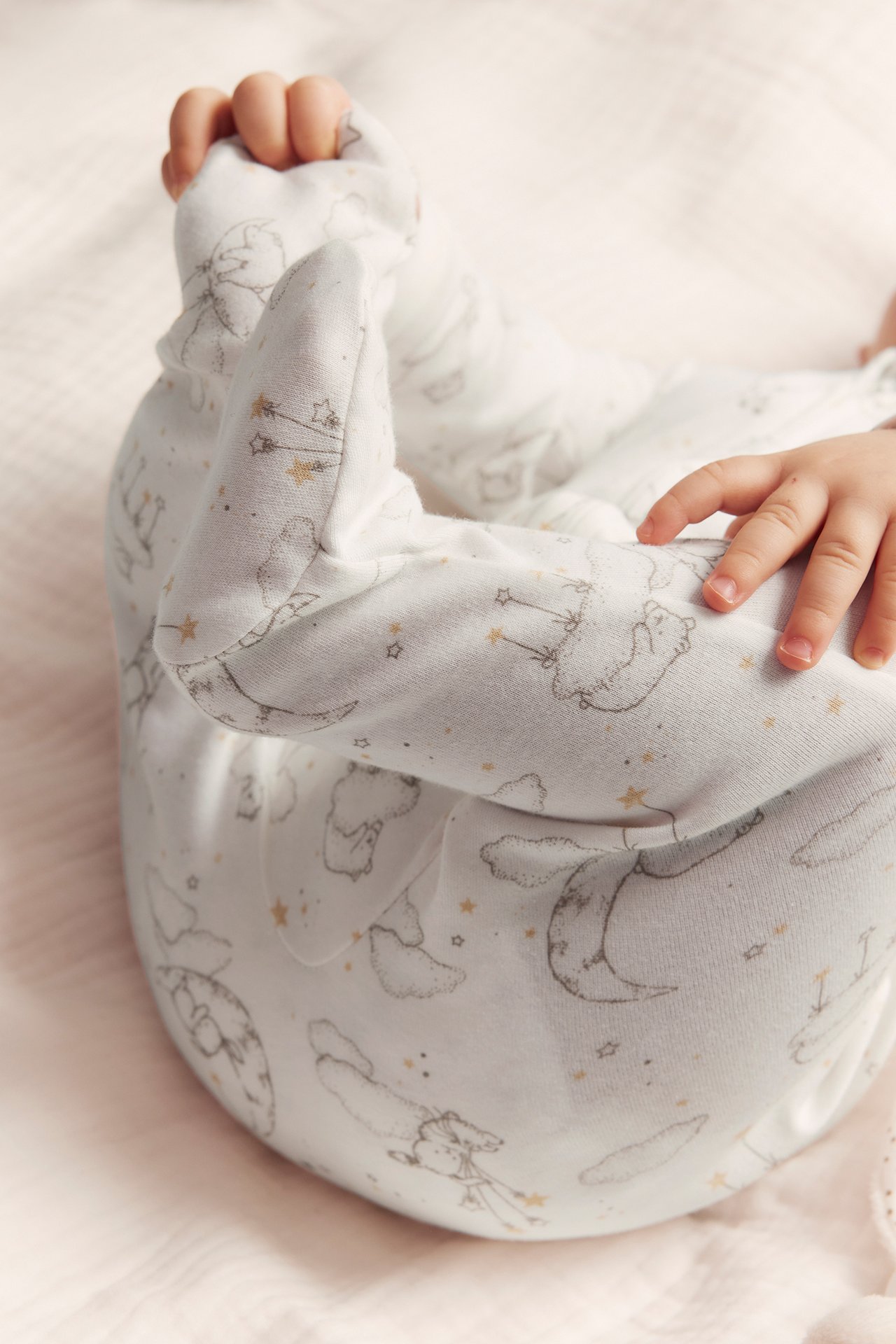 Close-up of a baby in an offwhite cotton pyjamas with grey animal, moon, star pattern and integrated feet.
