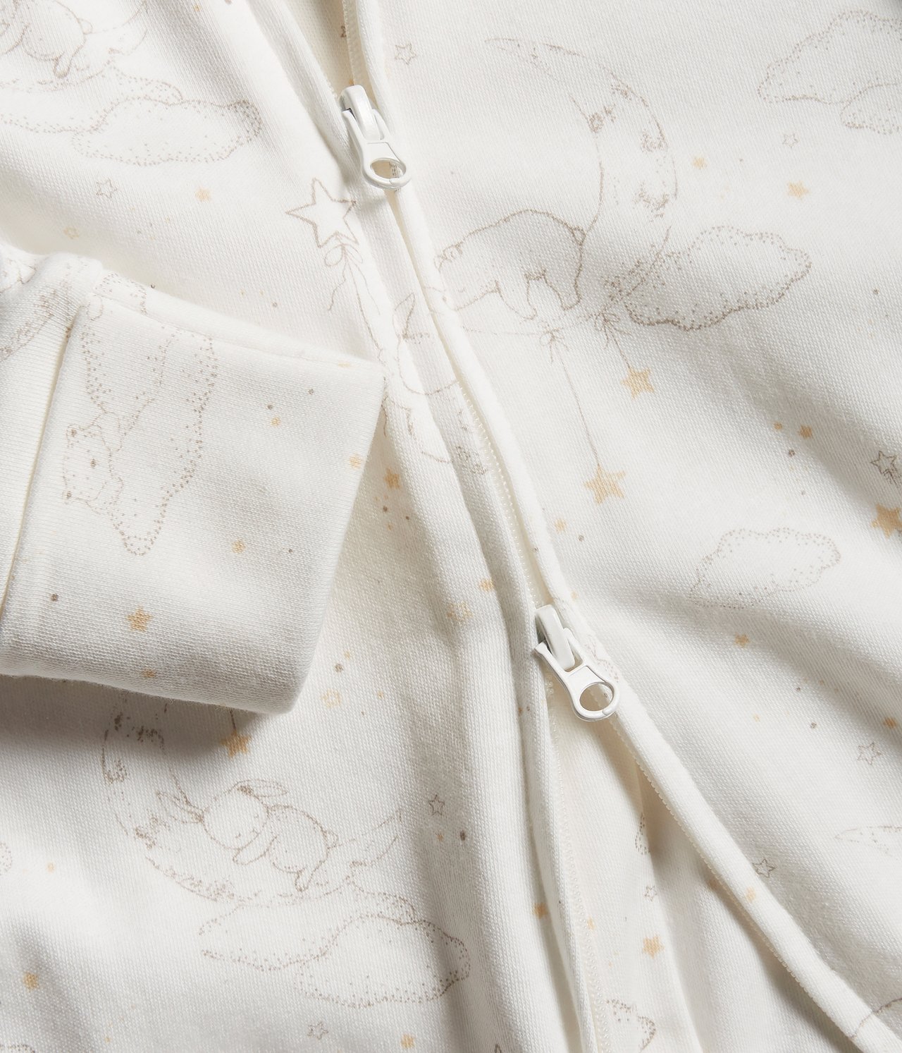 Close-up of off-white cotton baby pyjamas with two-way zipper and sleeping animal, moon, star pattern.