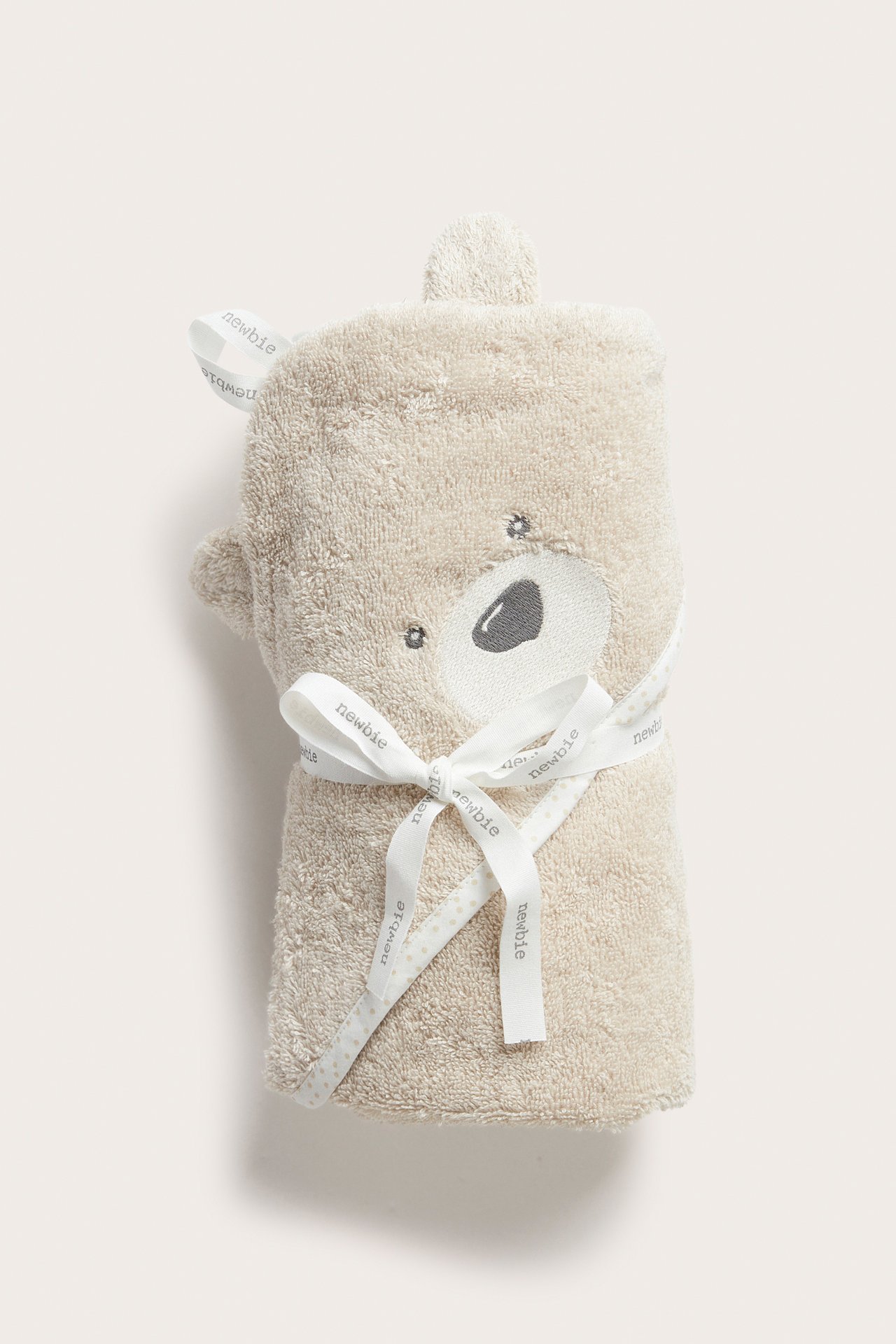 Front view: beige terry hooded baby bath towel with bear ears, embroidered face, tied with a ribbon.