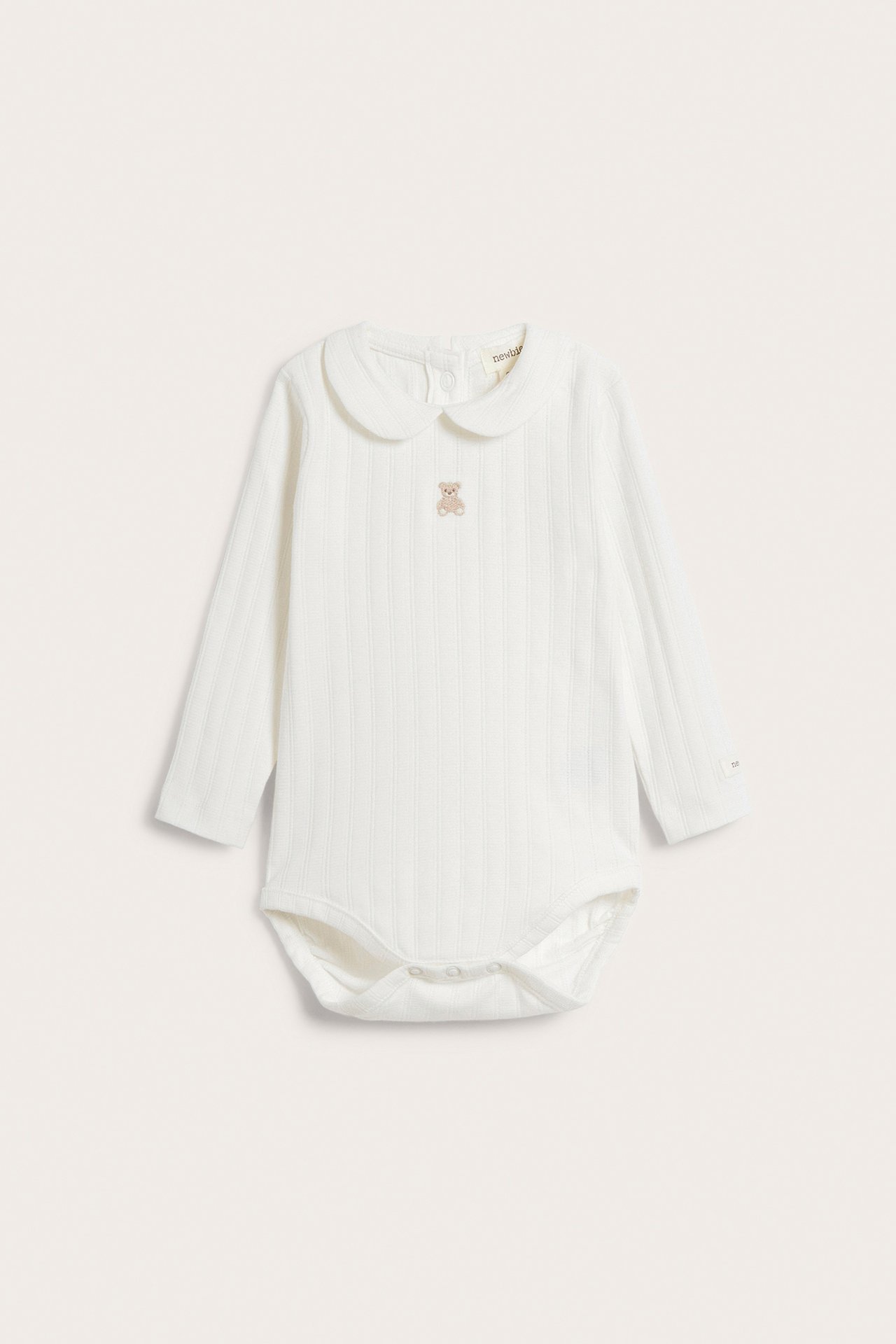 Vorderansicht eines cremeweißen langärmeligen Pointelle-Ripp-Babybodys mit Kragen und Teddybär-Stickerei.