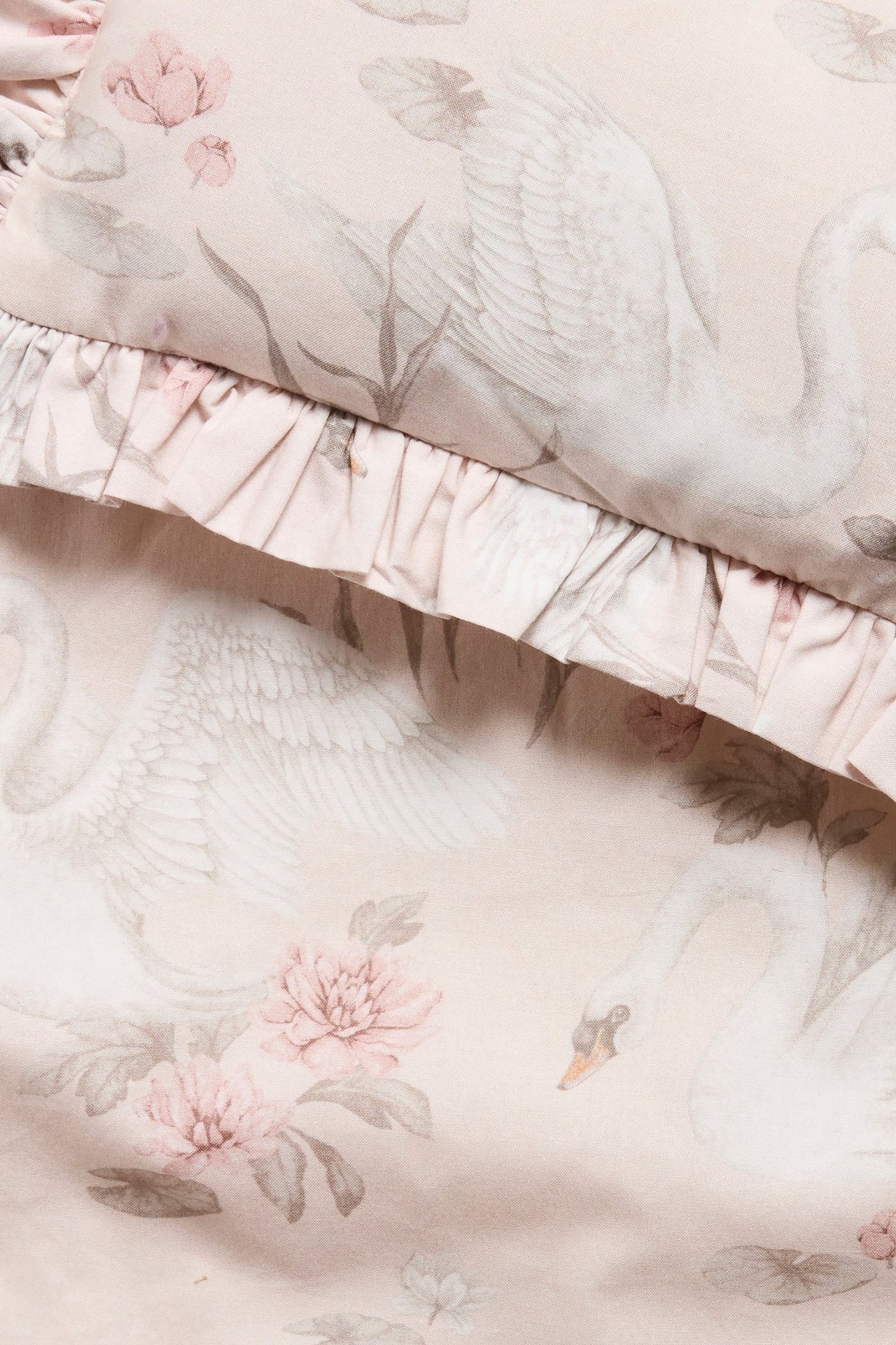 Nahaufnahme eines hellrosa Puppenbettwäsche-Sets mit weißem Schwanen- und rosa Blumenmuster, mit Rüschen.