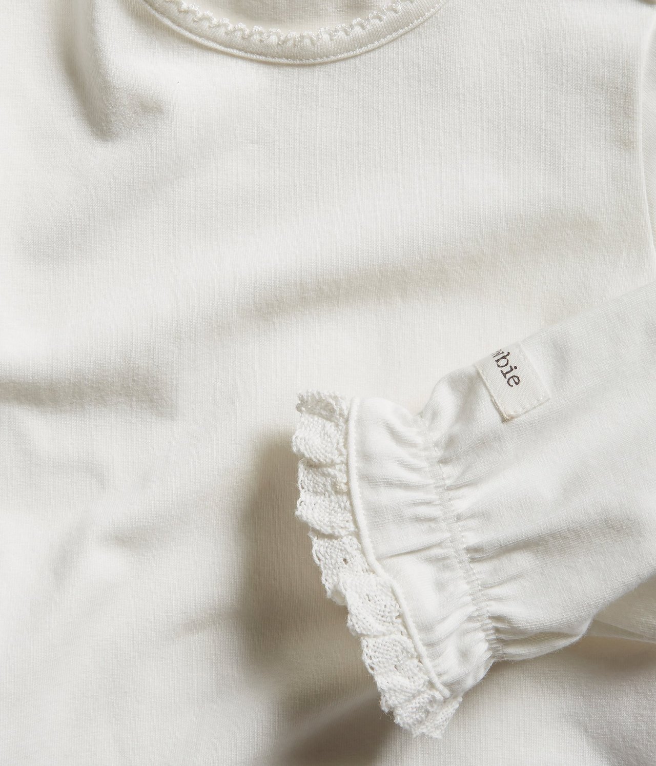 Close-up of an off-white long-sleeved baby bodysuit with picot neckline and ruffled lace cuffs.