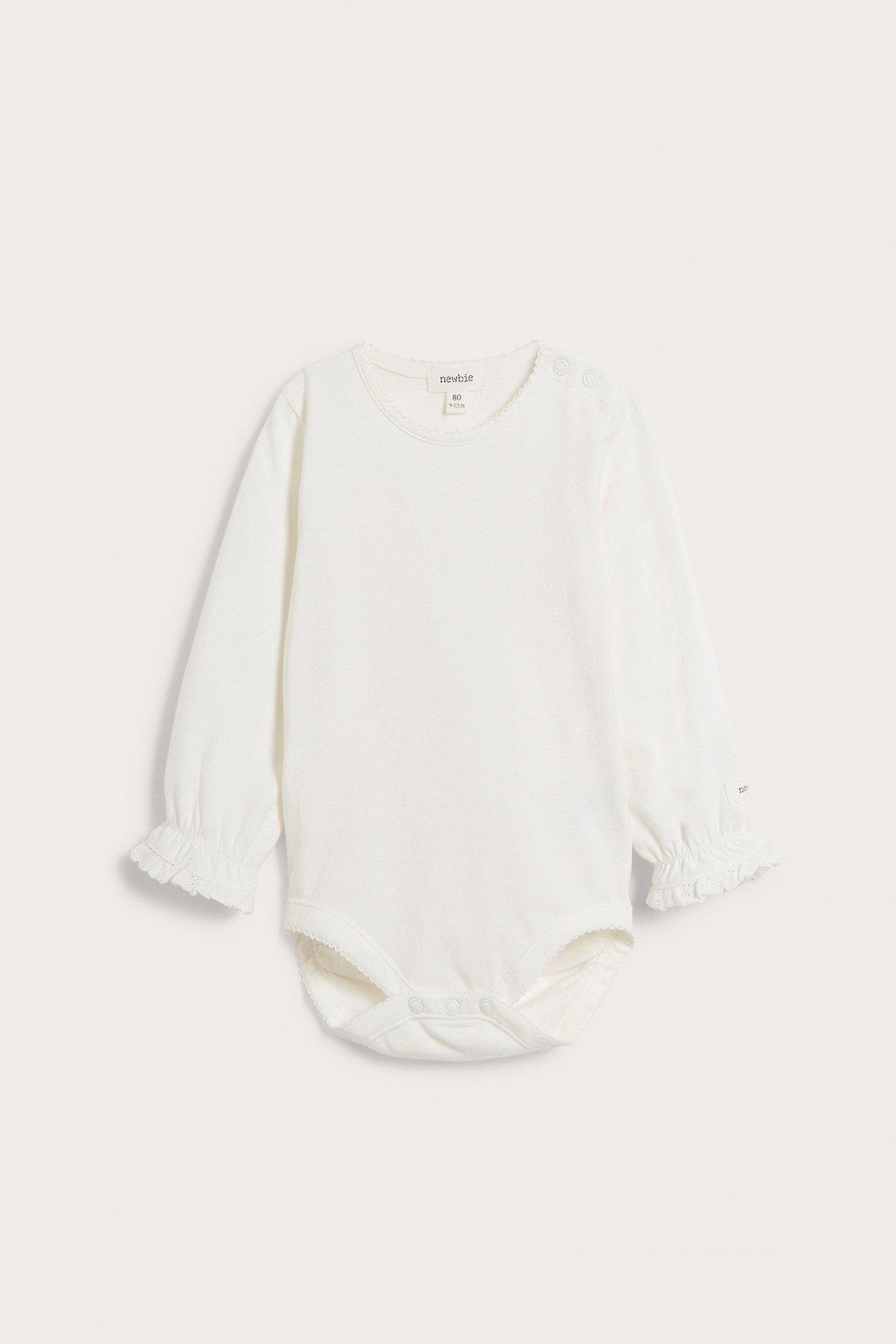 Front view of an off-white long-sleeved baby bodysuit with picot neckline, lace ruffle cuffs, and snap buttons.